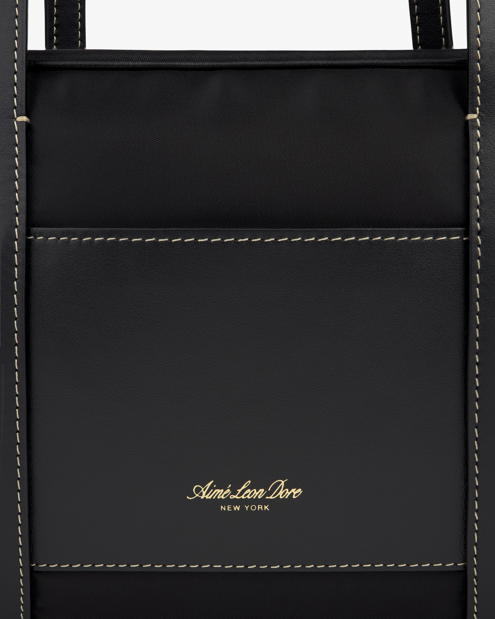 Close-up of a black Mini Duffle Shoulder Bag with white stitching and gold Aimé Leon Dore New York logo on the front pocket.
