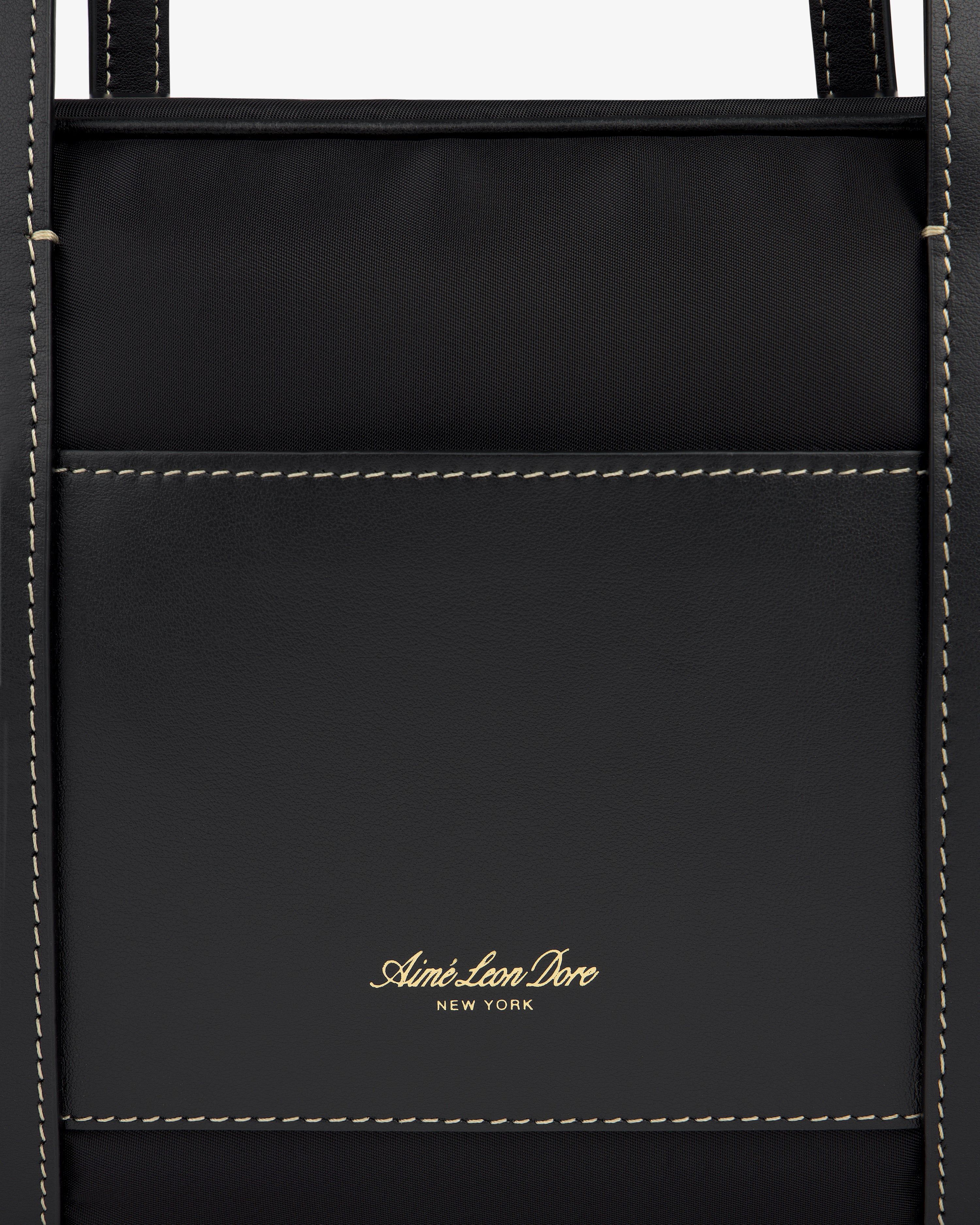 Close-up of a black Mini Duffle Shoulder Bag with white stitching and gold Aimé Leon Dore New York logo on the front pocket.
