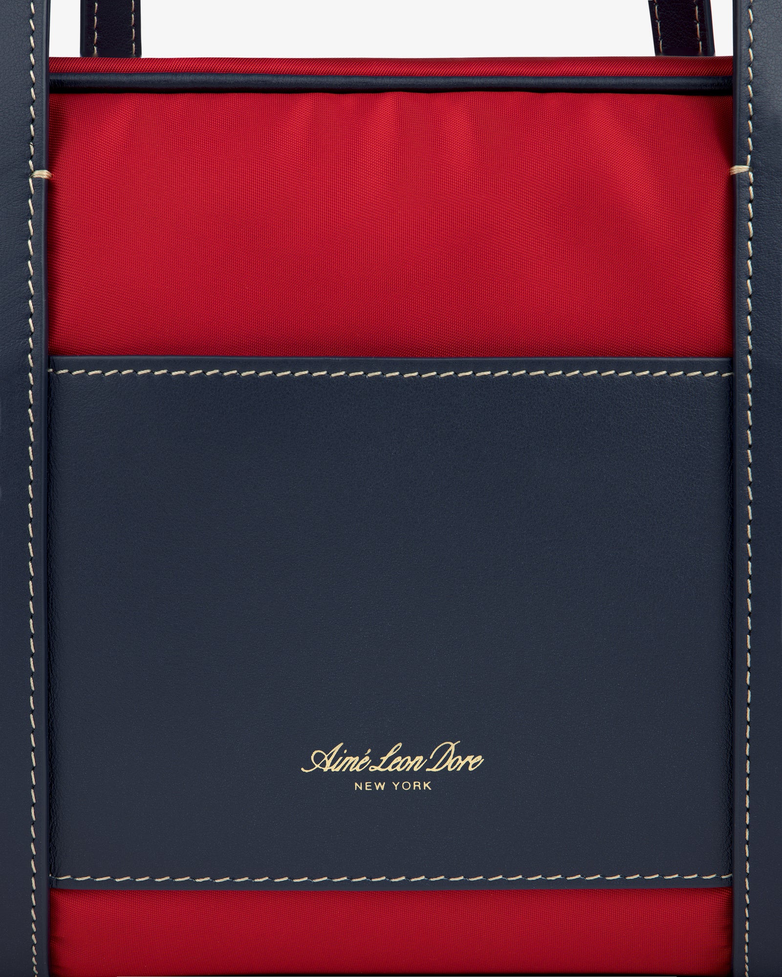 Close-up of a red and navy Mini Duffle Shoulder Bag with white stitching and gold Aimé Leon Dore New York text.