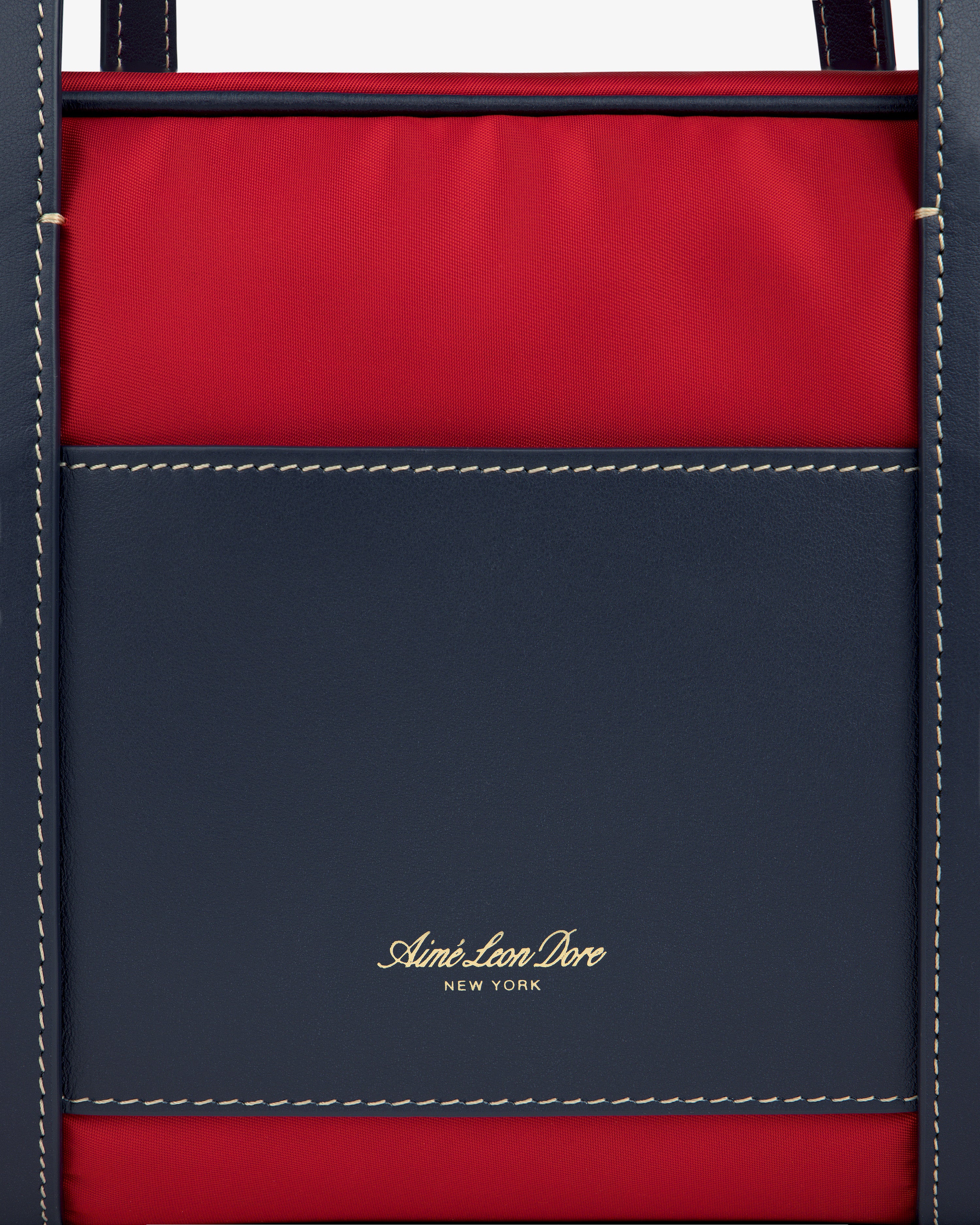 Close-up of a red and navy Mini Duffle Shoulder Bag with white stitching and gold Aimé Leon Dore New York text.