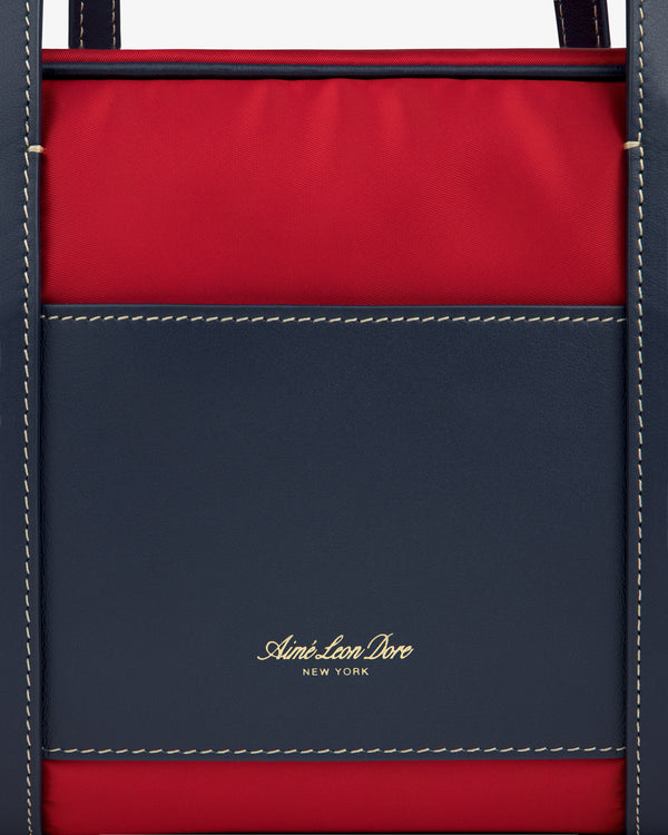 Close-up of a red and navy Mini Duffle Shoulder Bag with white stitching and gold Aimé Leon Dore New York text.