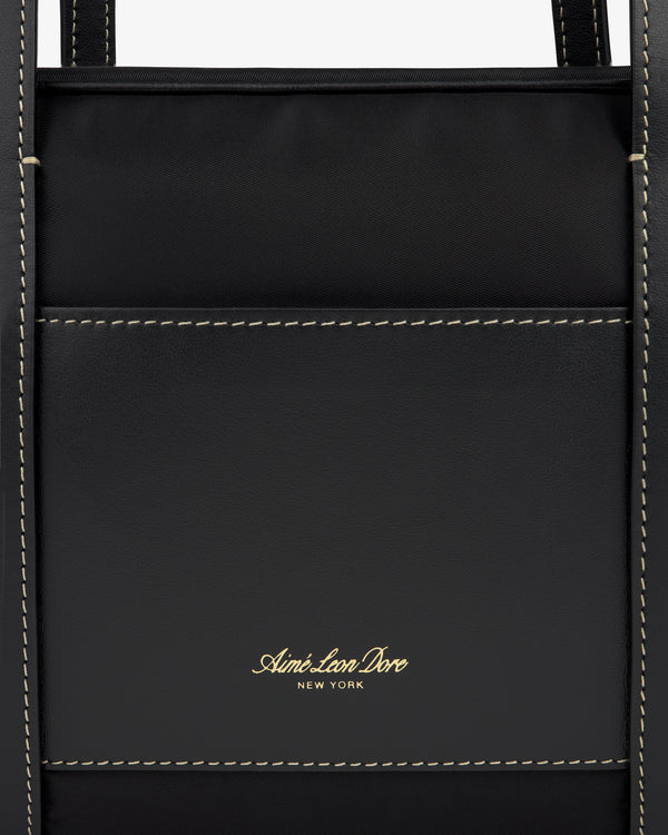Close-up of a black Mini Duffle Shoulder Bag with white stitching and gold Aimé Leon Dore New York logo on the front pocket.