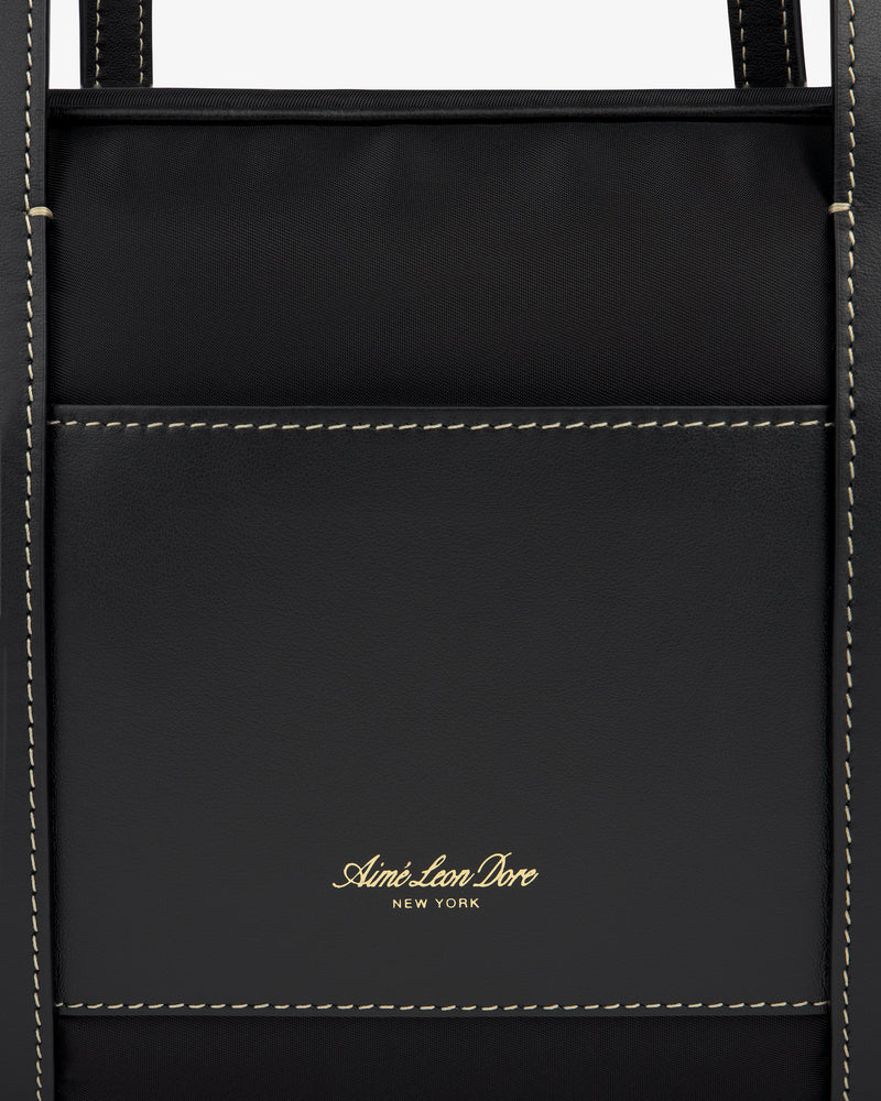 Close-up of a black Mini Duffle Shoulder Bag with white stitching and gold Aimé Leon Dore New York logo on the front pocket.
