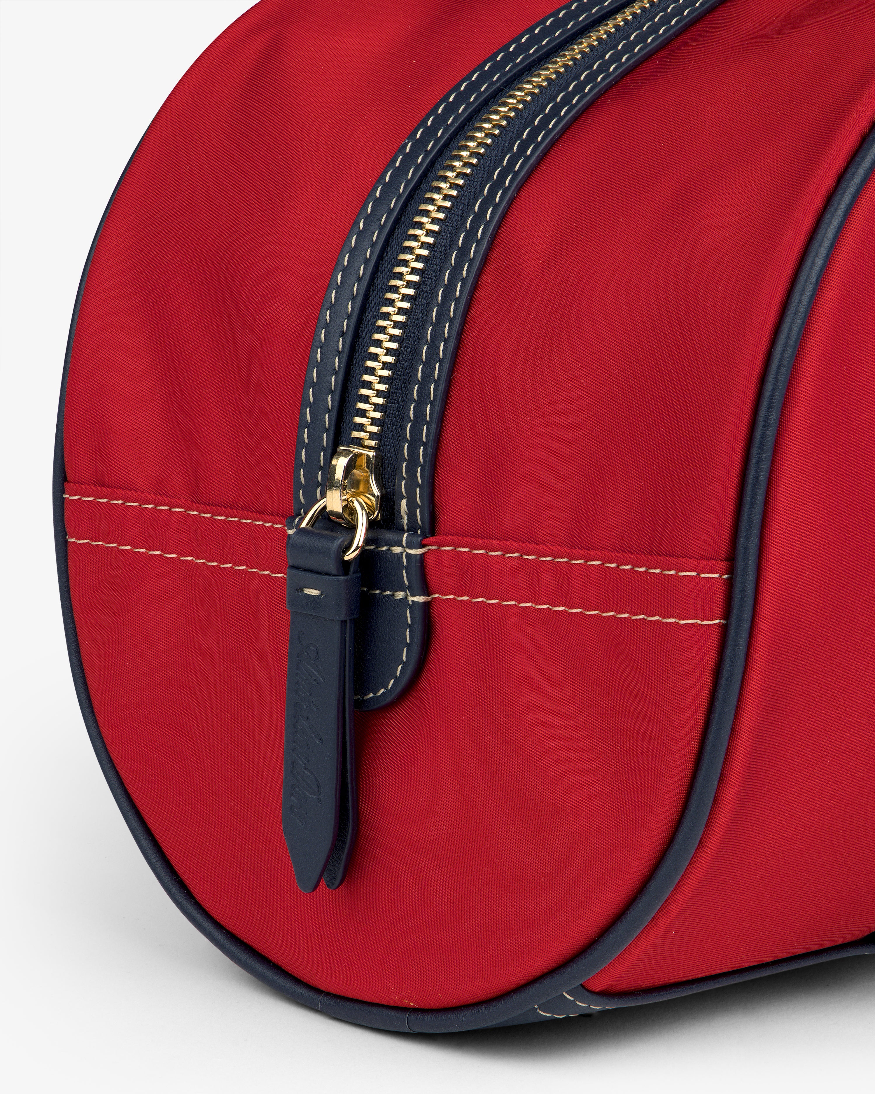 Close-up of the Mini Duffle Shoulder Bag: red with a gold zipper, navy trim, and white stitching on a light background.