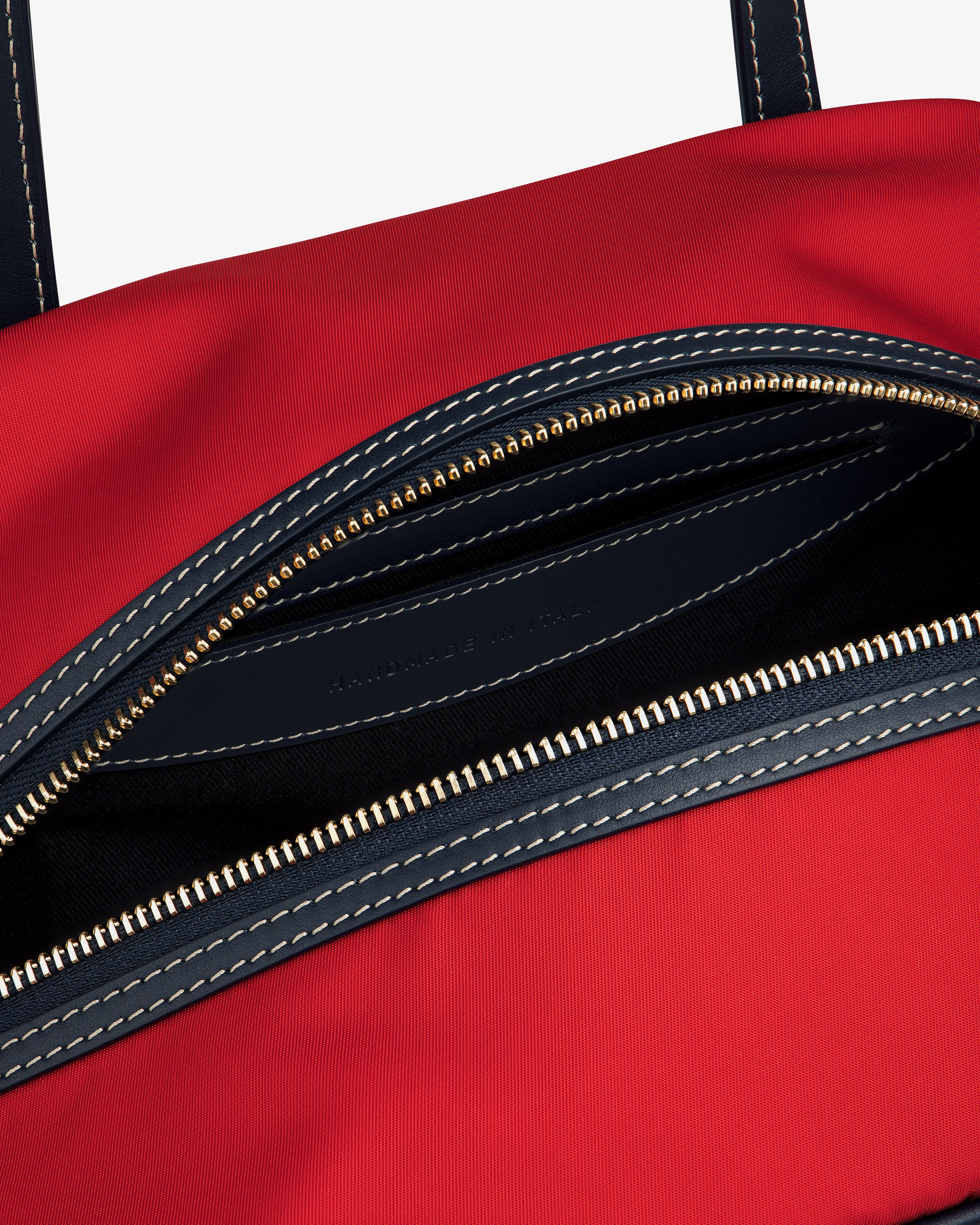 Close-up of Mini Duffle Shoulder Bag: open red design, gold zipper, black lining, and white stitched details.
