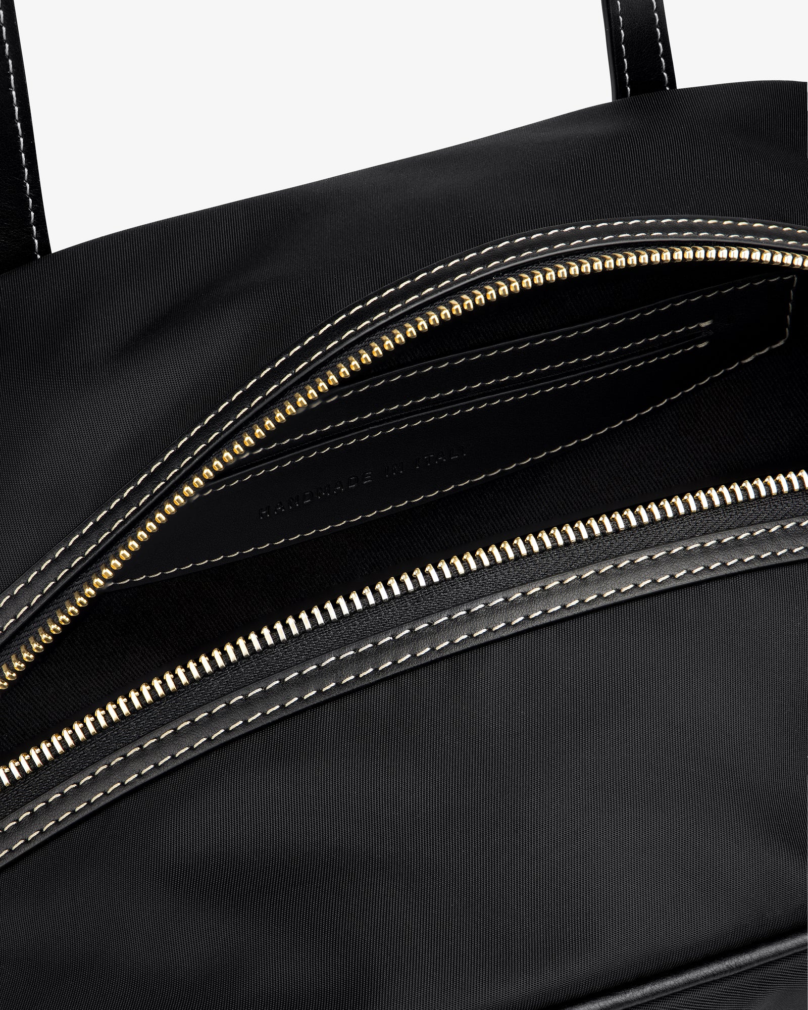Close-up of the Mini Duffle Shoulder Bag in black with a gold zipper and white stitching, partially open to reveal interior.
