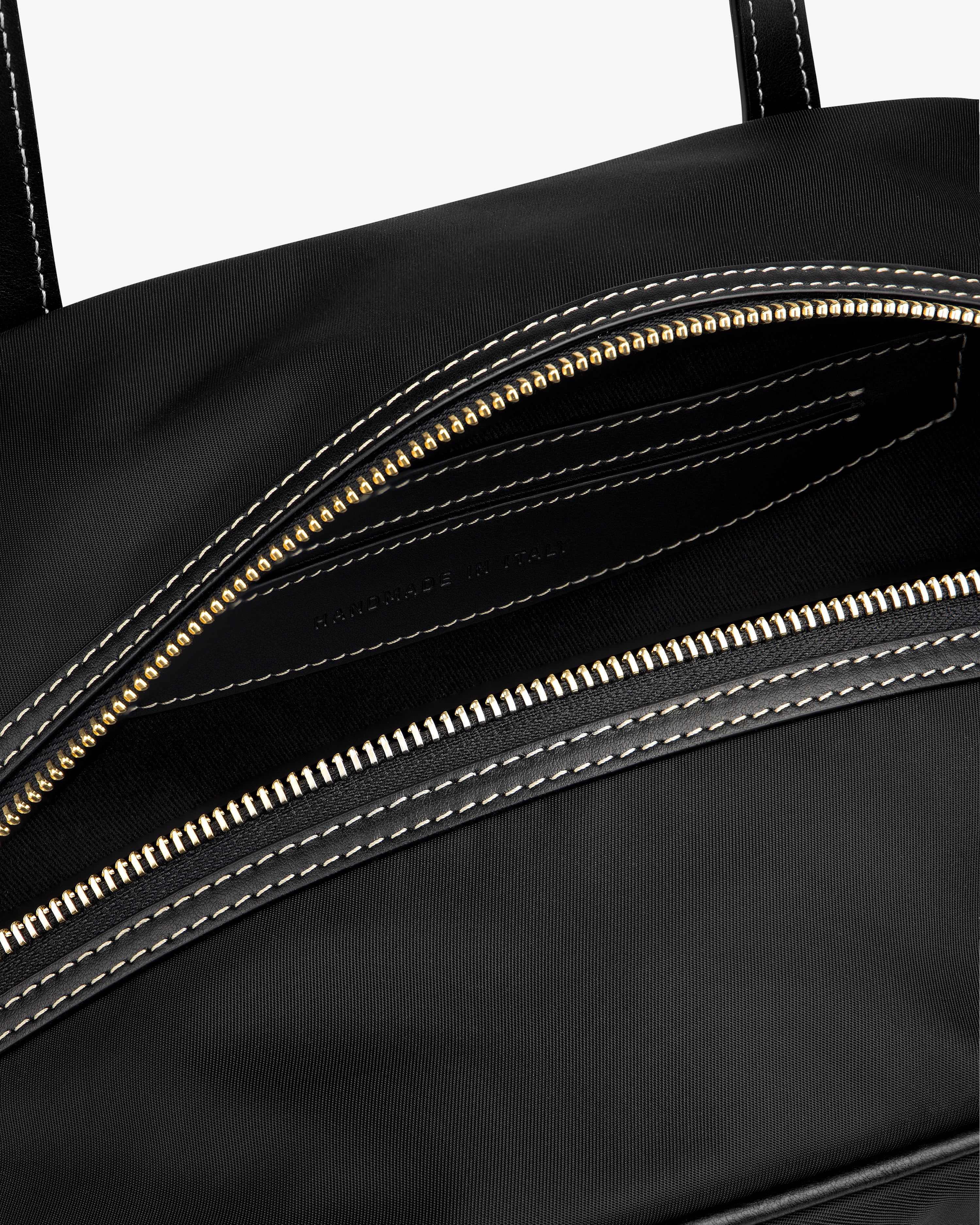 Close-up of the Mini Duffle Shoulder Bag in black with a gold zipper and white stitching, partially open to reveal interior.