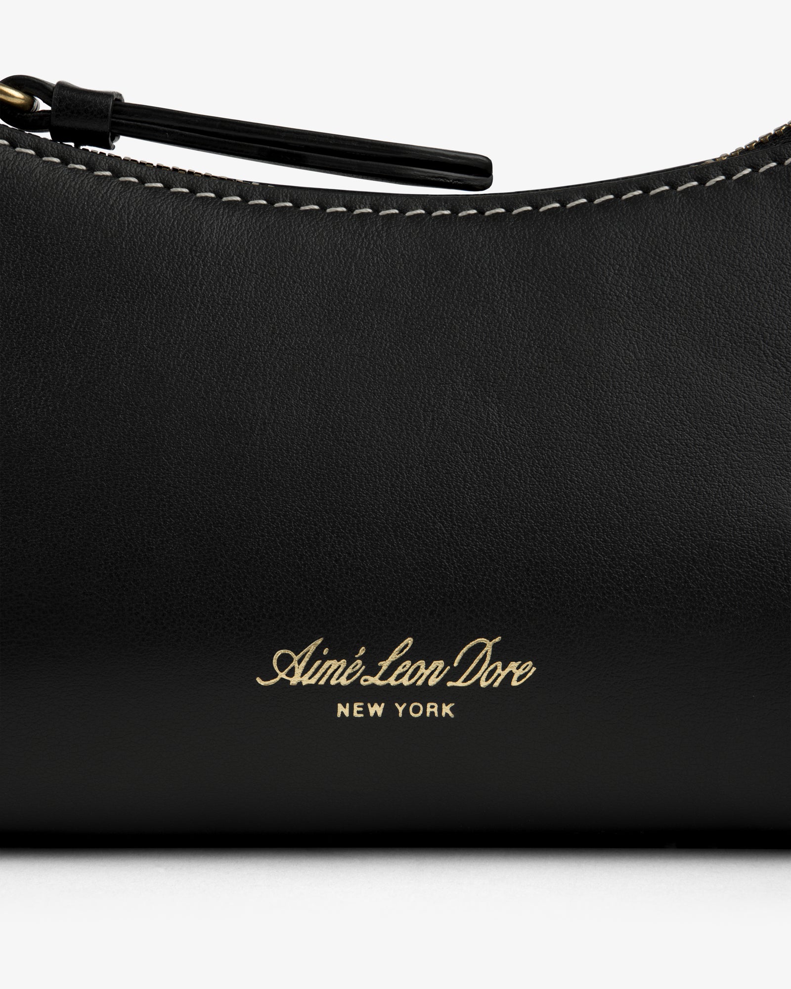 Close-up of the Convertible Leather Belt Bag in black leather with Aimé Leon Dore New York gold text and white stitching.