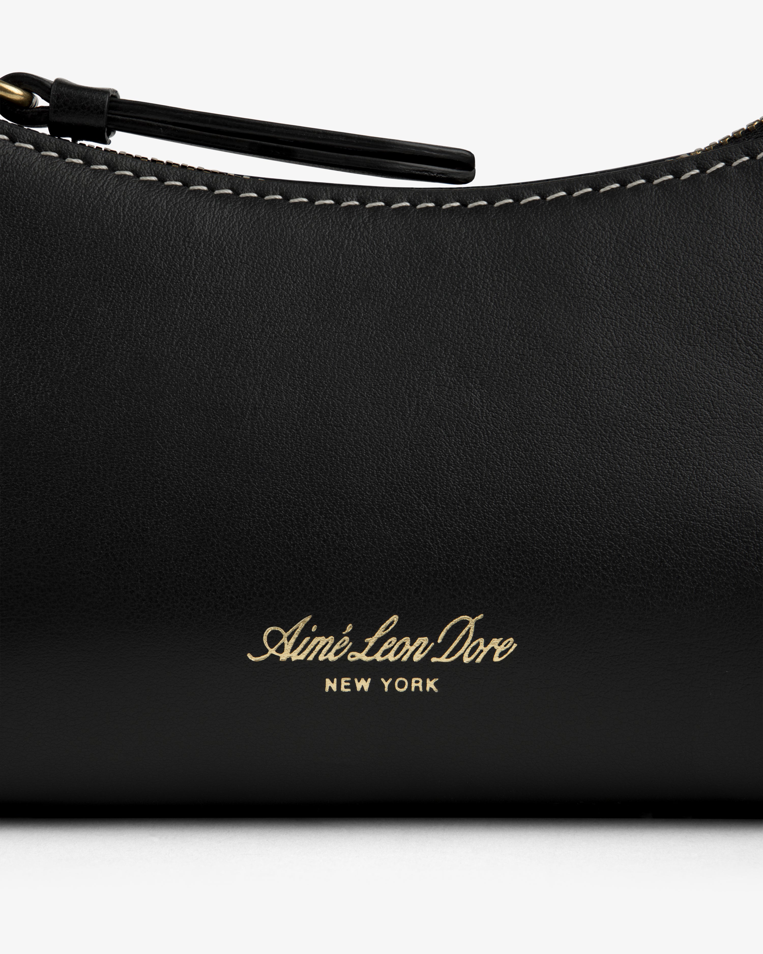 Close-up of the Convertible Leather Belt Bag in black leather with Aimé Leon Dore New York gold text and white stitching.
