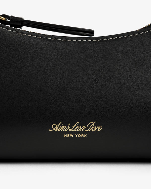 Close-up of the Convertible Leather Belt Bag in black leather with Aimé Leon Dore New York gold text and white stitching.