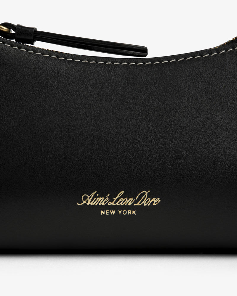 Close-up of the Convertible Leather Belt Bag in black leather with Aimé Leon Dore New York gold text and white stitching.