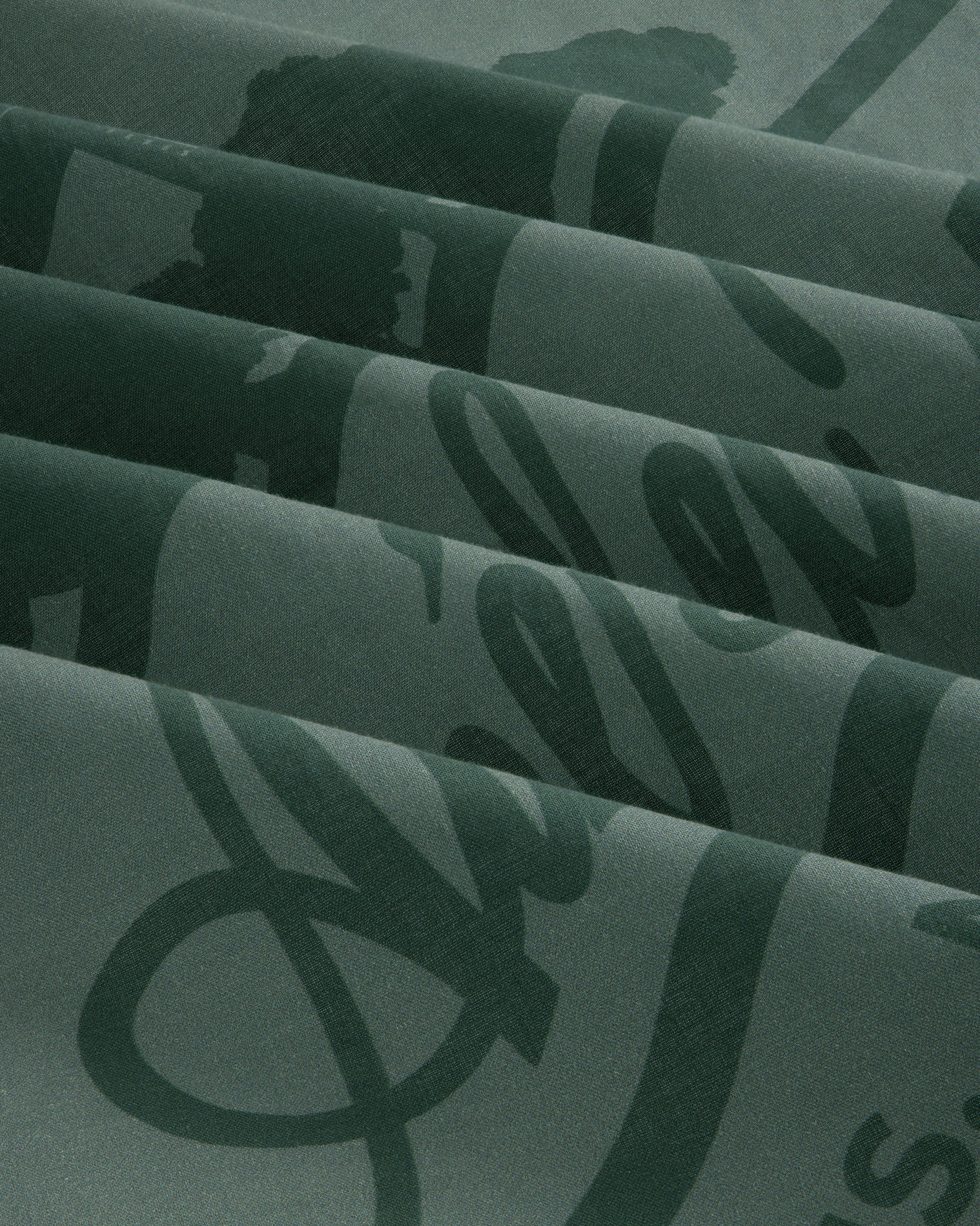 Sun Faded Unisphere Bandana in dark green with shiny cursive script, folded in neat pleats.