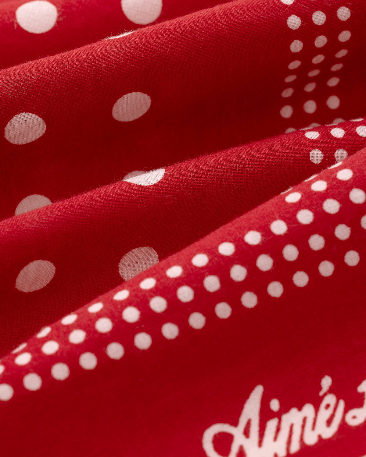 Red Polka Dot Bandana with white script "Aimé" partially visible at the bottom right corner.