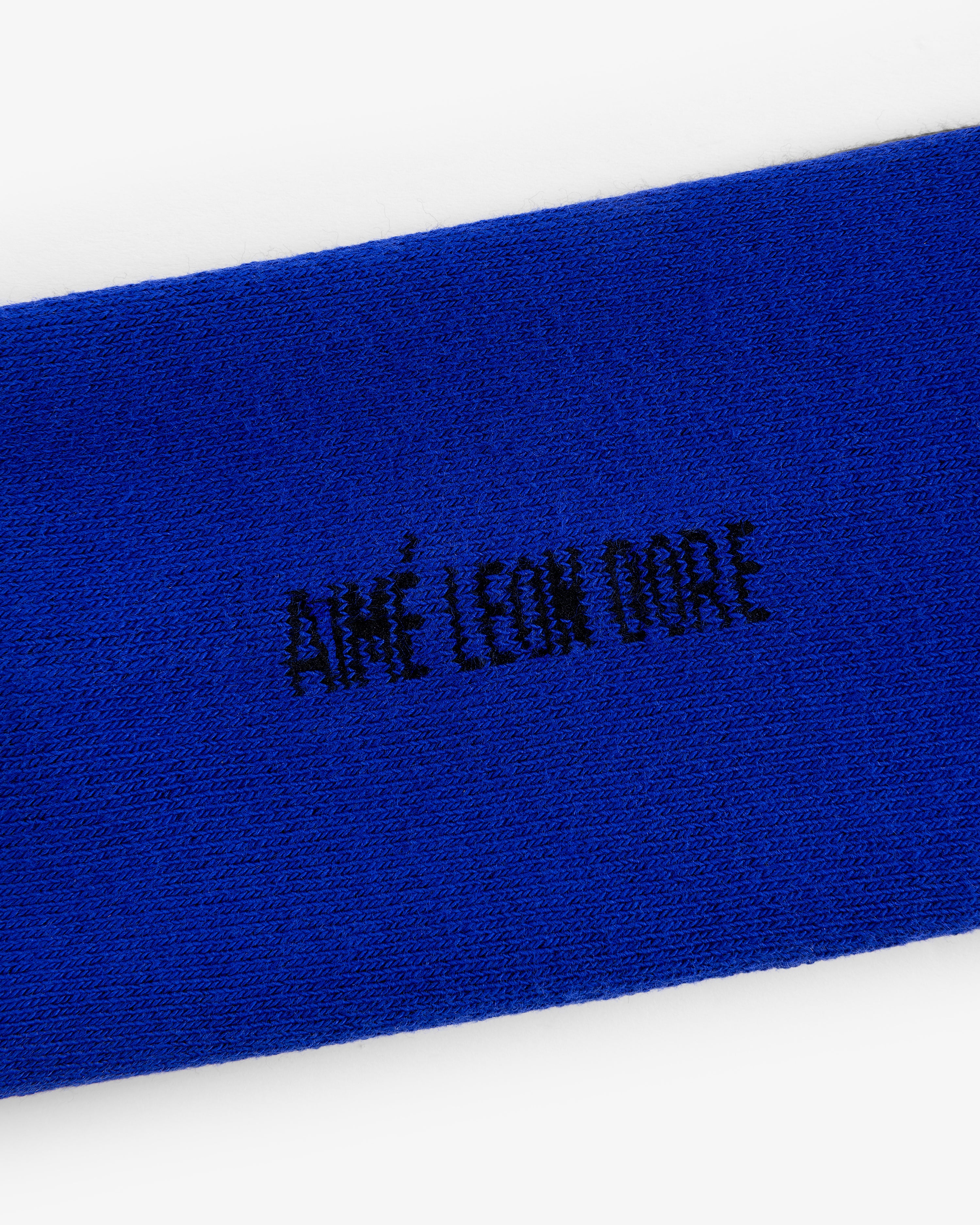 Close-up of blue Crew Sock 3-Pack with AIMÉ LEON DORE embroidered in black, all-capital letters.