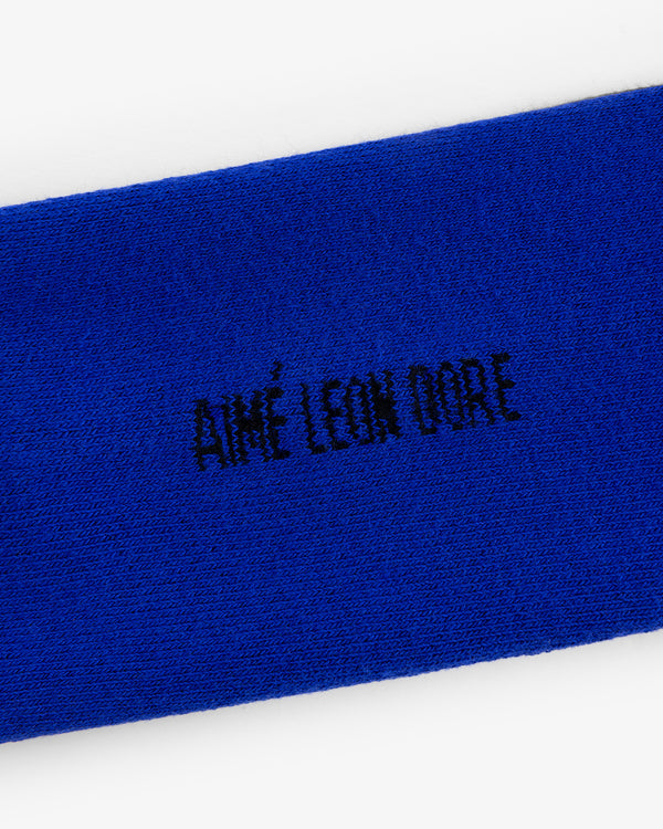 Close-up of blue Crew Sock 3-Pack with AIMÉ LEON DORE embroidered in black, all-capital letters.