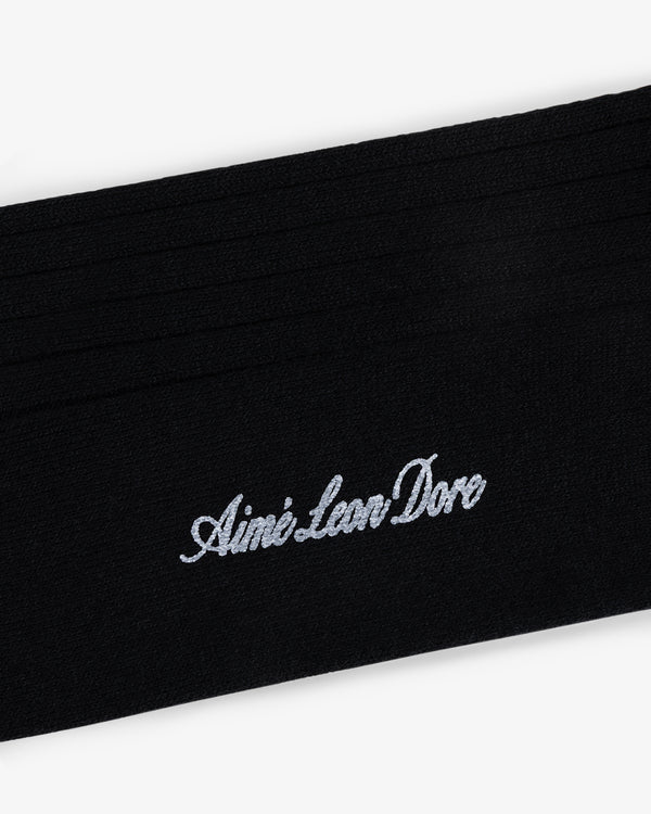 Close-up of black Dress Sock with Aimé Leon Dore embroidered in white cursive text.