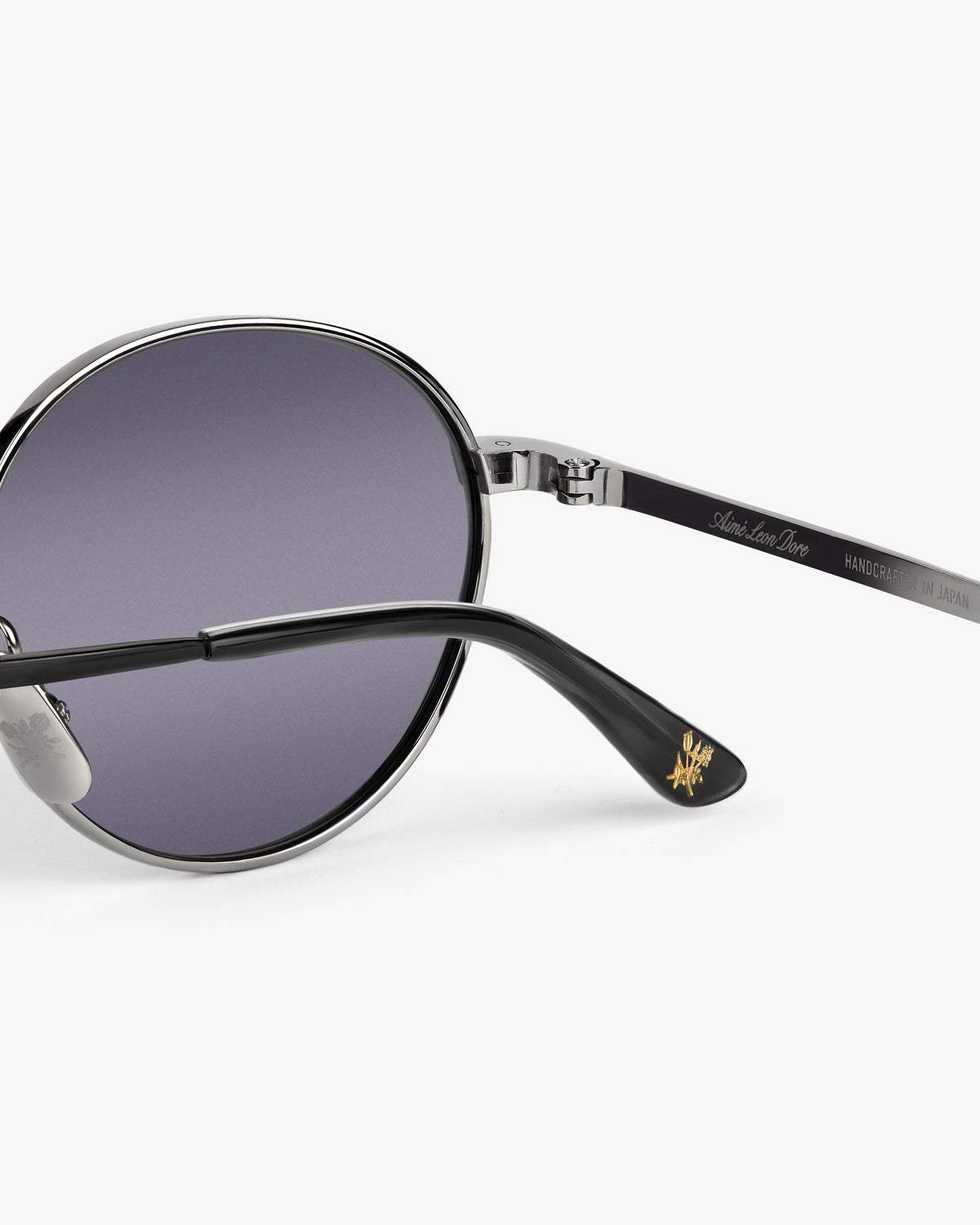 Close-up of Giórgios Sunglasses with a silver frame, purple lenses, and gold logo on the black arm tip.