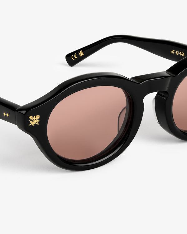 Onásis Sunglasses: Black round frames with pink-tinted lenses and gold detailing on the temples and frame.