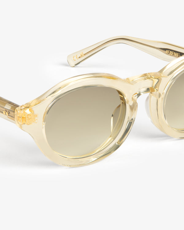 Close-up of Onásis Sunglasses featuring stylish round clear beige frames and brown gradient lenses on a white background.