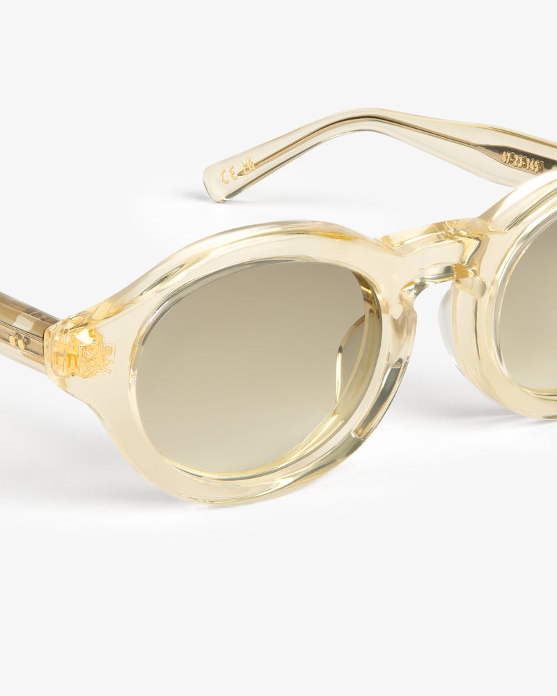 Close-up of Onásis Sunglasses featuring stylish round clear beige frames and brown gradient lenses on a white background.