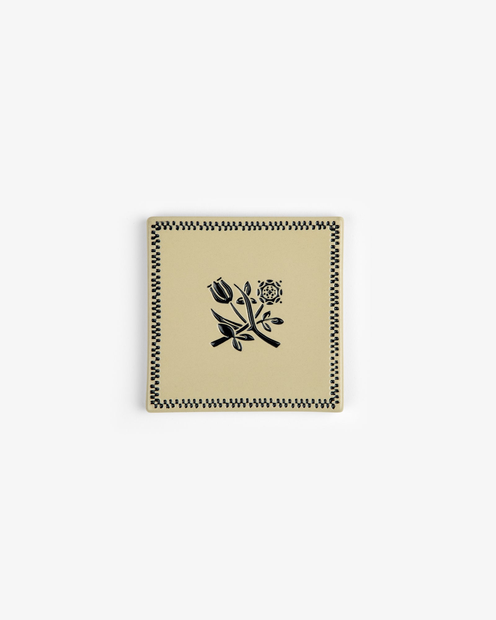 The Crest Coaster (Set of 4) features square beige ceramic pieces with black floral and checkered designs.