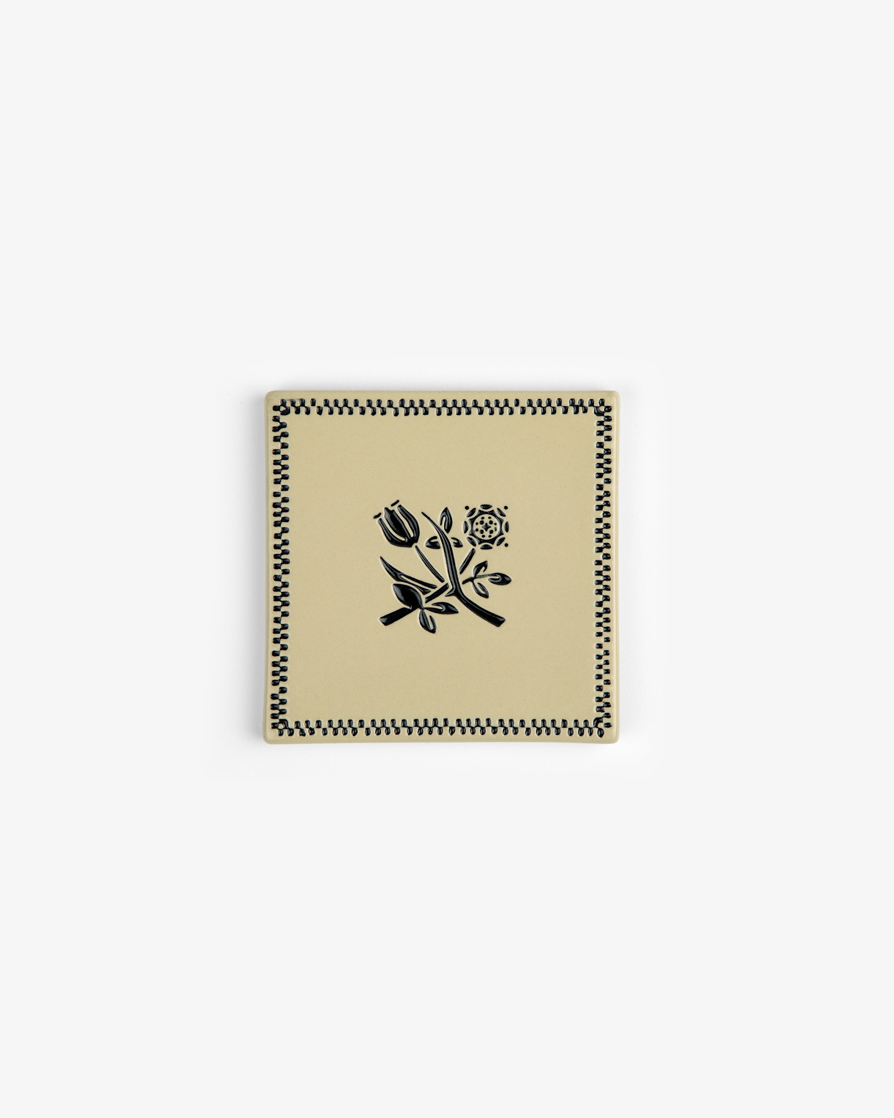 The Crest Coaster (Set of 4) features square beige ceramic pieces with black floral and checkered designs.