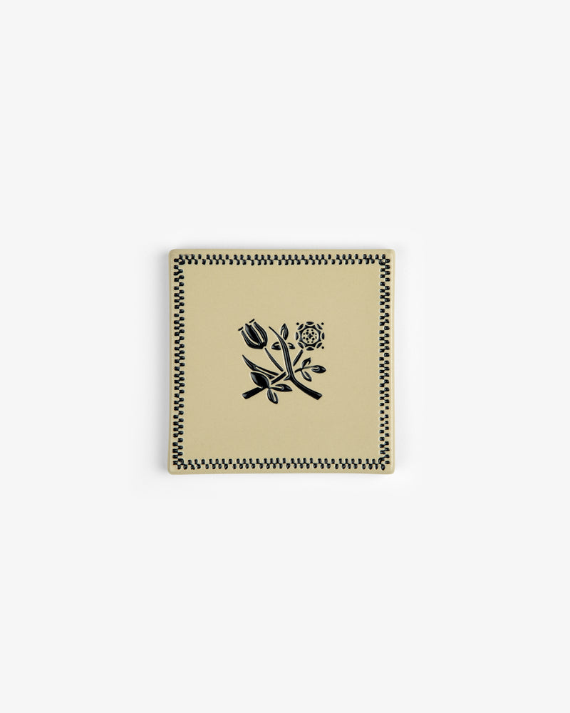 The Crest Coaster (Set of 4) features square beige ceramic pieces with black floral and checkered designs.