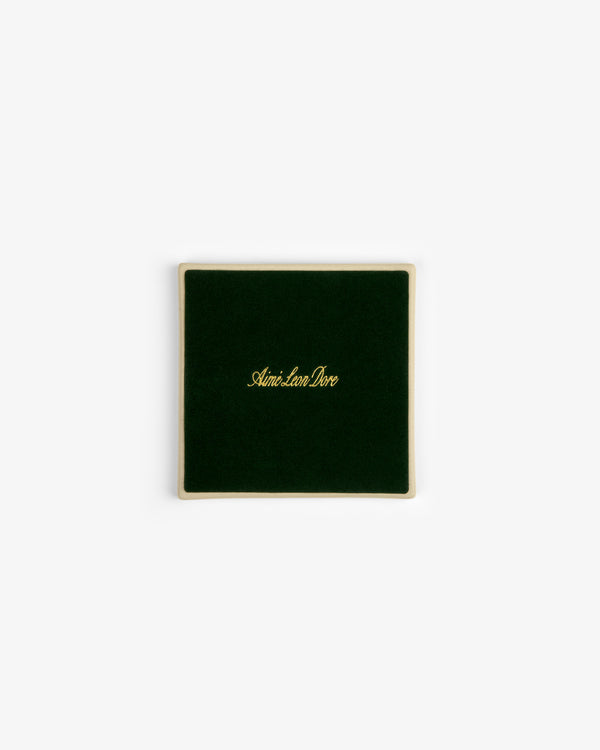 A square green velvet case with gold trim, holding Crest Coaster (Set of 4), Aimé Leon Dore in gold on lid.