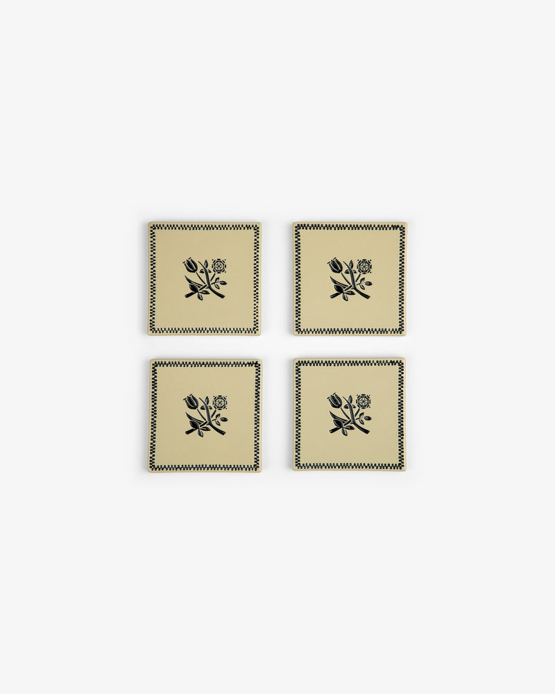 The Crest Coaster Set (4 pcs) features beige coasters with black floral designs and zigzag borders, arranged in a grid.