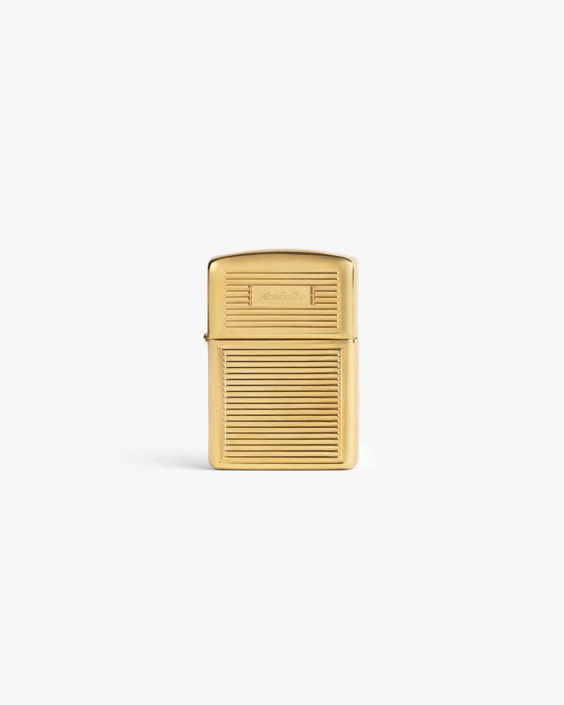 A brass Zippo lighter with a ridged body and smooth lid stands upright on a white background.