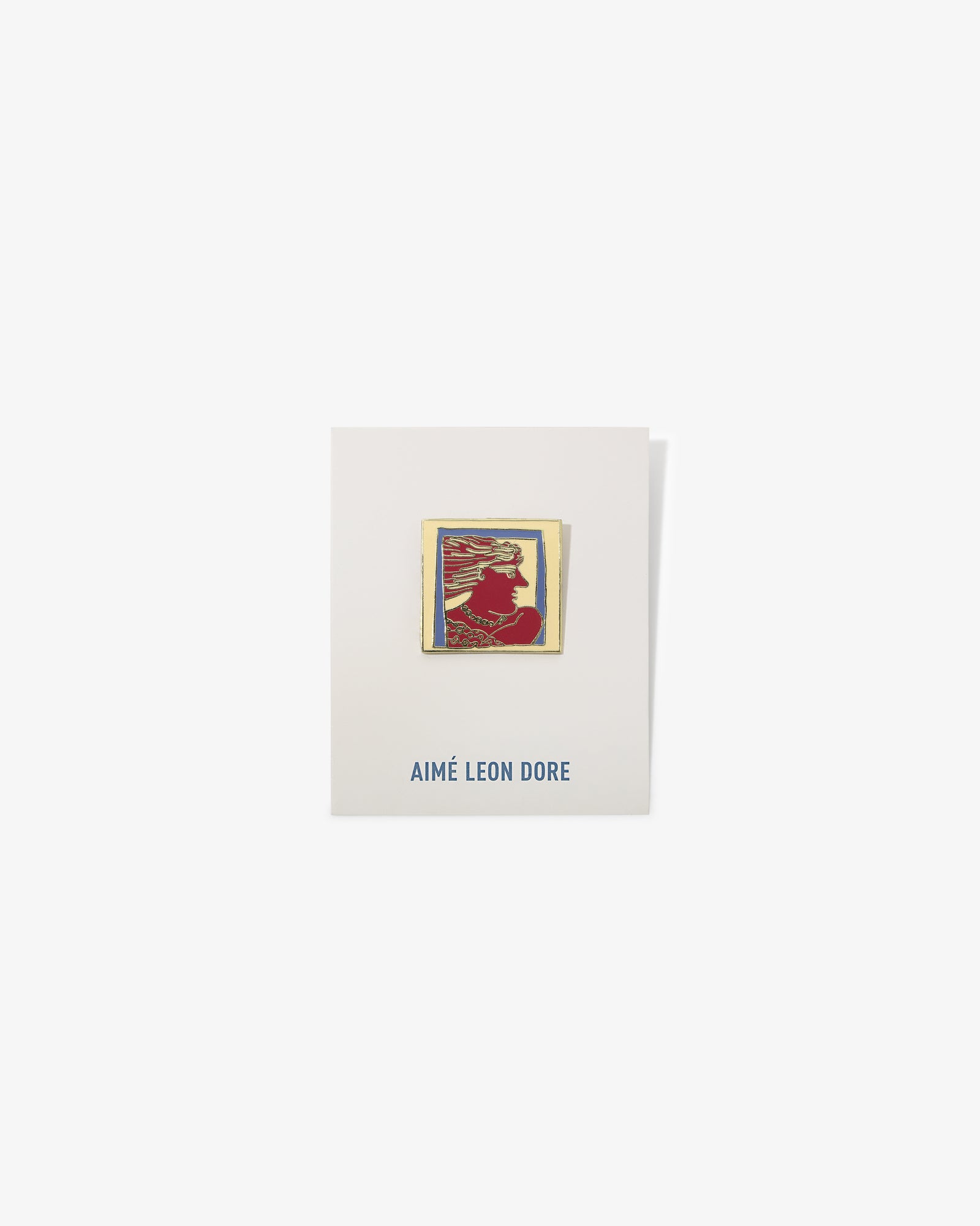 A gold-framed red and yellow Graphic Pin with a silhouette on a white AIMÉ LEON DORE card.