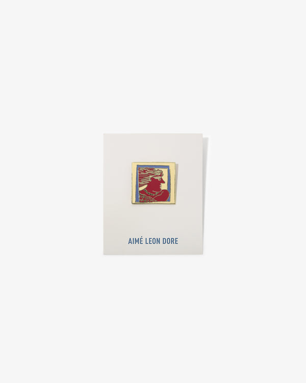 A gold-framed red and yellow Graphic Pin with a silhouette on a white AIMÉ LEON DORE card.