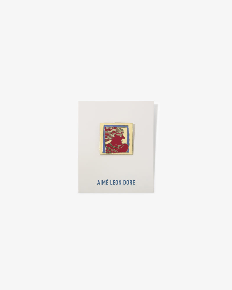 A gold-framed red and yellow Graphic Pin with a silhouette on a white AIMÉ LEON DORE card.