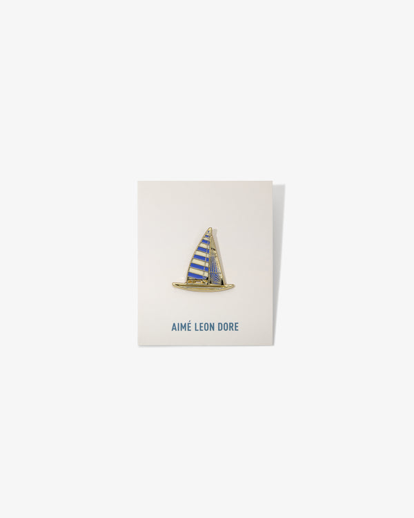 A gold and blue Graphic Pin shaped like a sailboat on a white AIMÉ LEON DORE card.