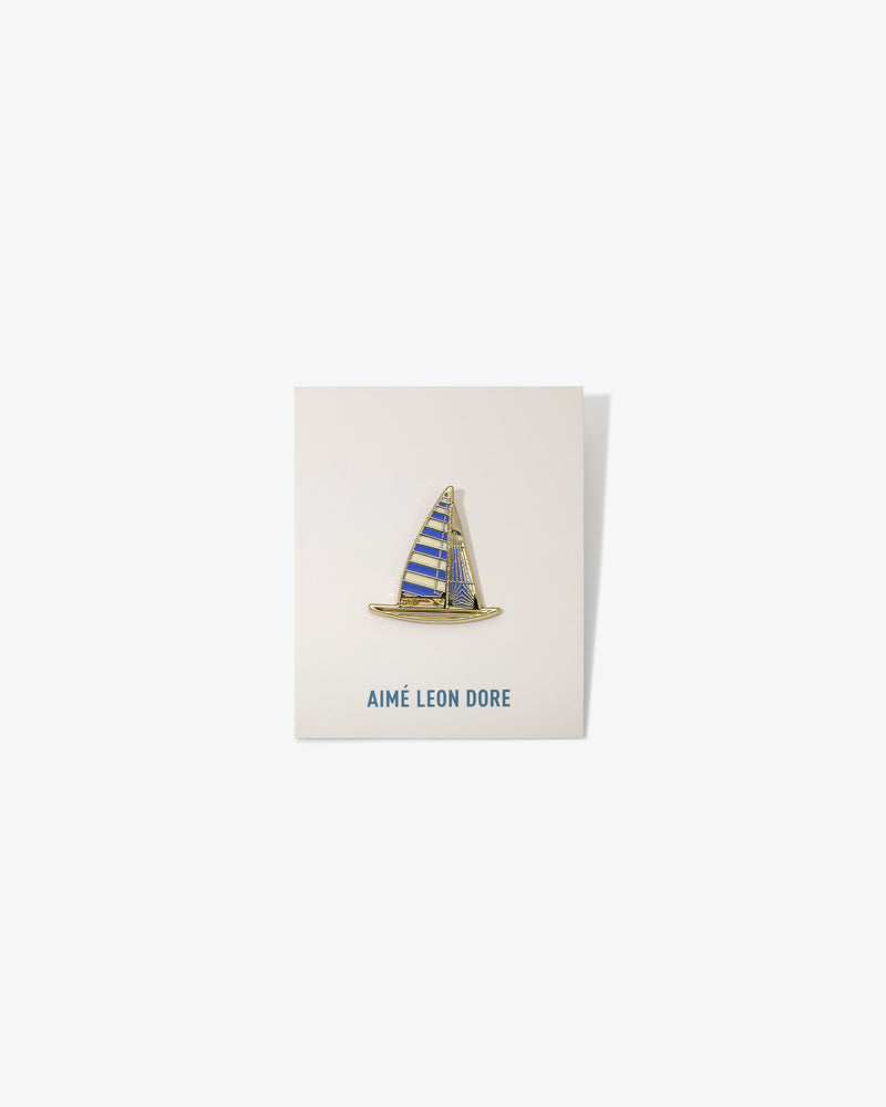 A gold and blue Graphic Pin shaped like a sailboat on a white AIMÉ LEON DORE card.