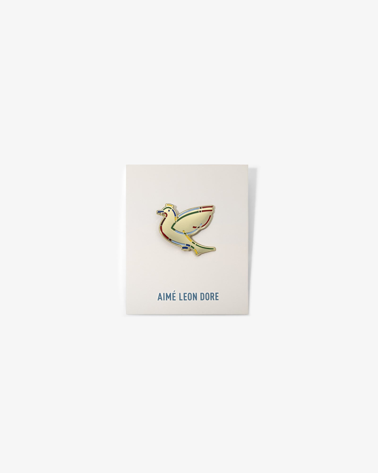 The Graphic Pin, a gold bird-shaped enamel pin, is shown on a white card labeled AIMÉ LEON DORE.