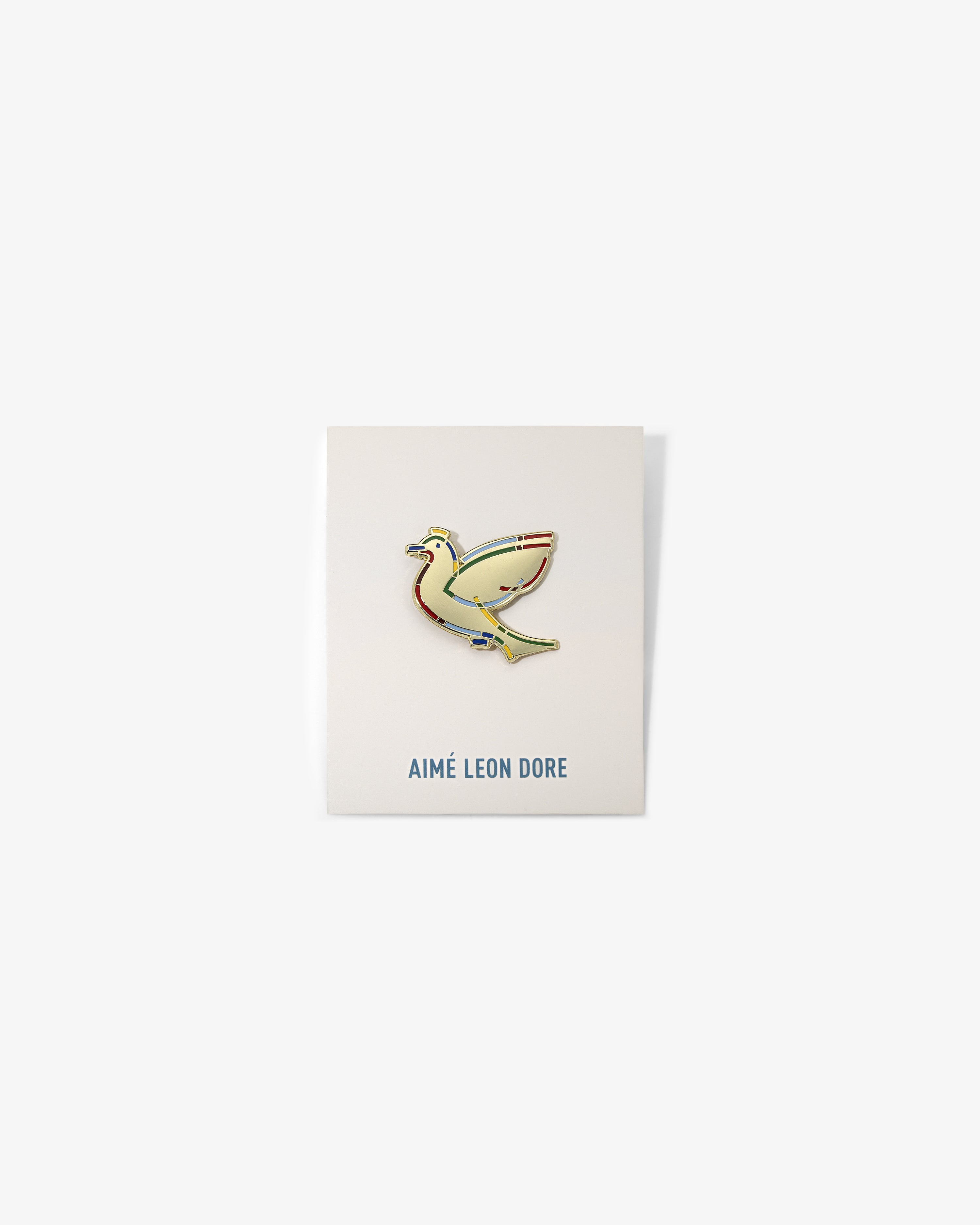 The Graphic Pin, a gold bird-shaped enamel pin, is shown on a white card labeled AIMÉ LEON DORE.