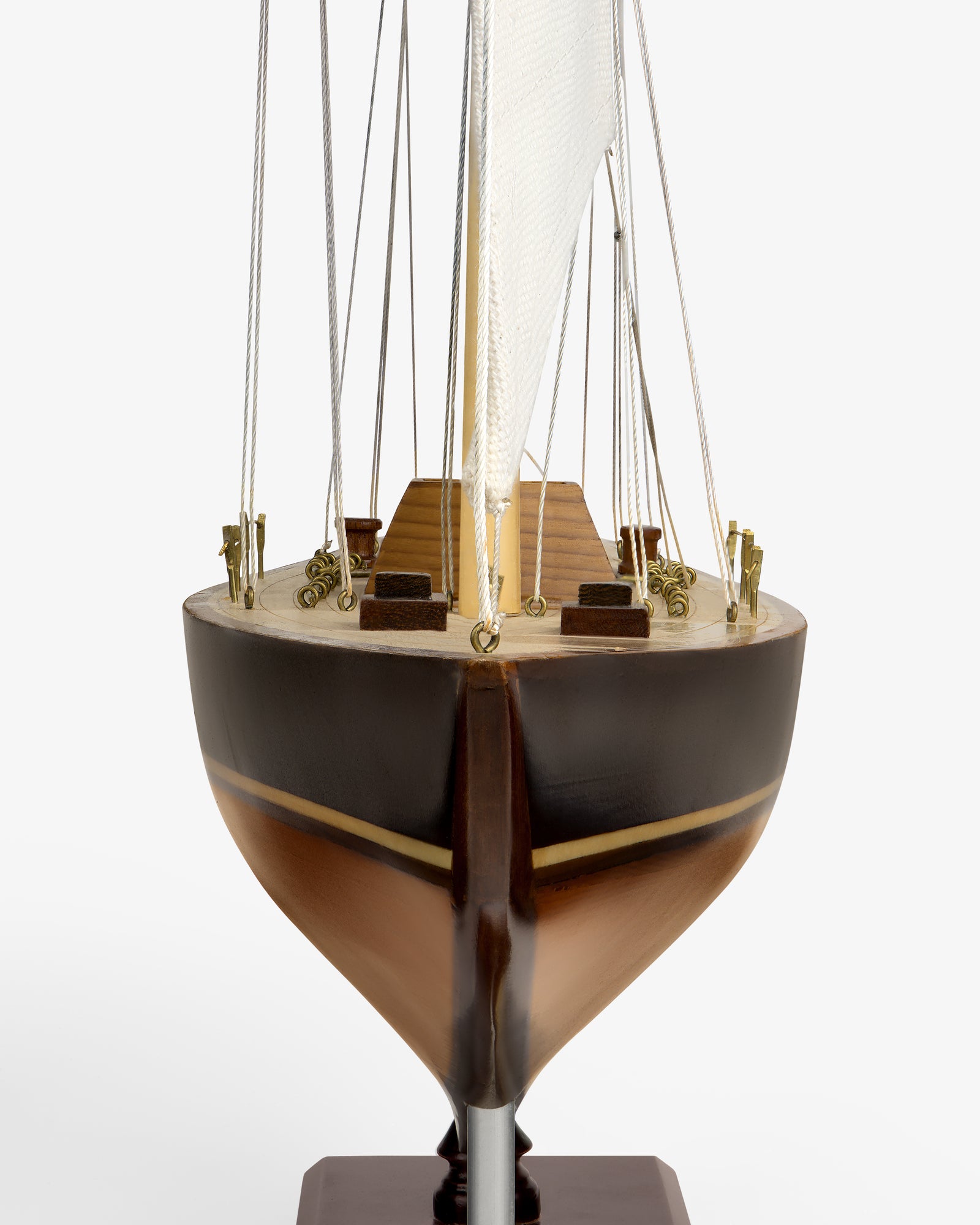 Walnut Model Sailboat viewed from the front, featuring a brown hull, deck details, and a white sail with rigging.
