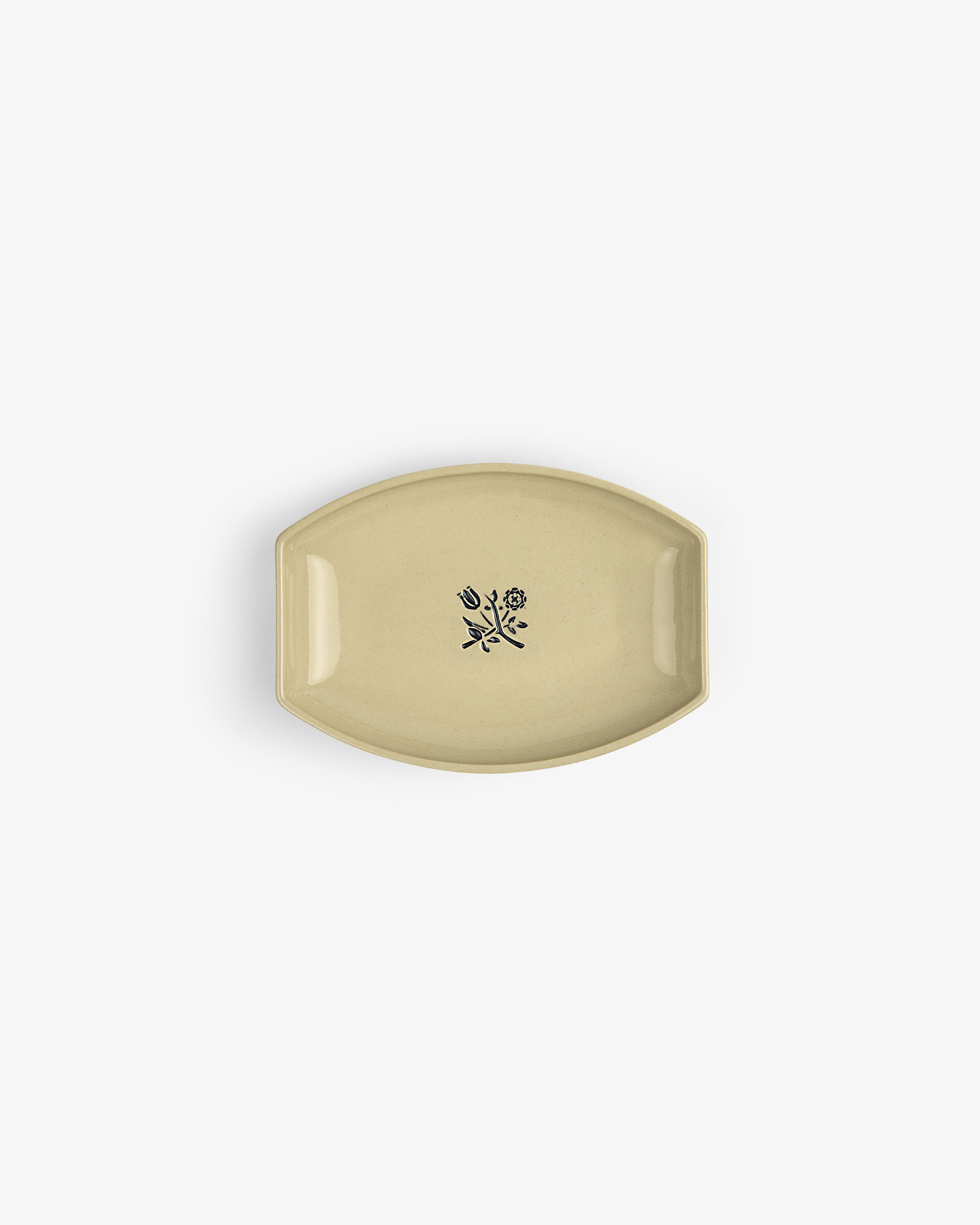 The Crest Catchall: a small beige ceramic dish with a black floral design at its center, shown from above.