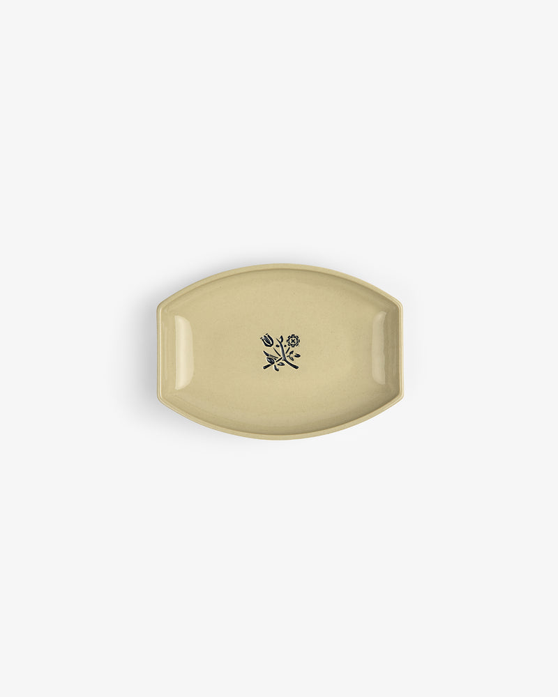 The Crest Catchall: a small beige ceramic dish with a black floral design at its center, shown from above.