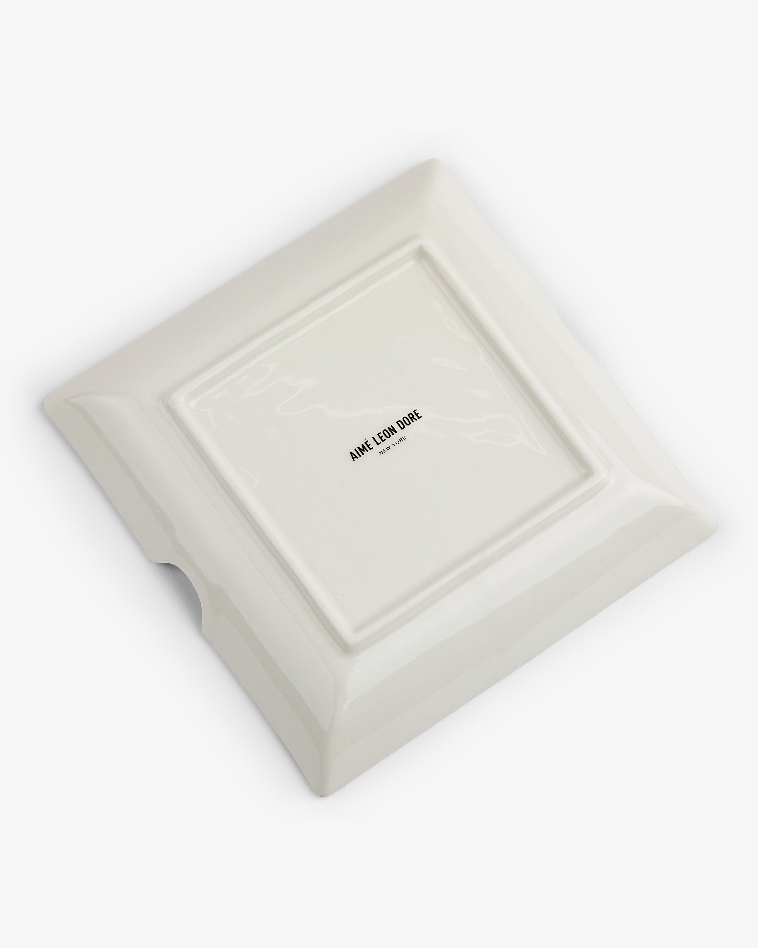 A white, square ceramic Fassianos "Nocturnal Love" Ashtray upside down shows its logo at the center of the base.