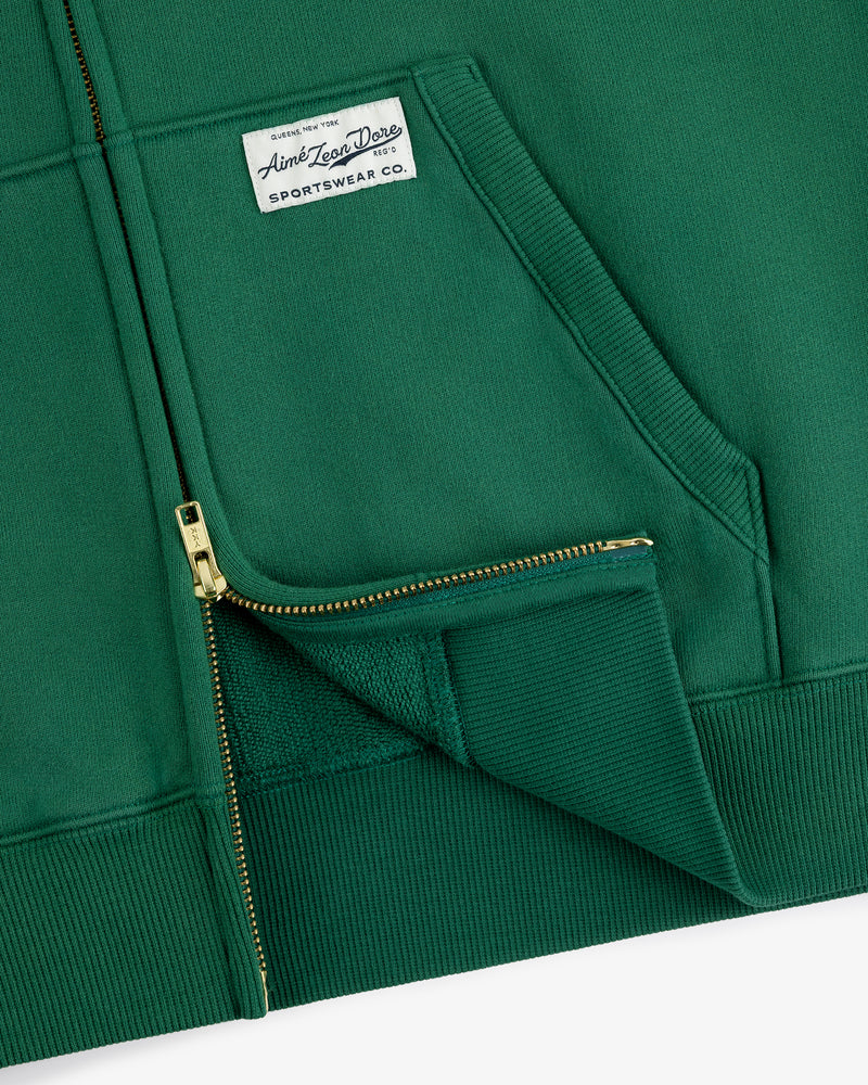 Sun Faded Full-Zip Hoodie in green with front pockets and a white Aimé Leon Dore patch on the left chest.