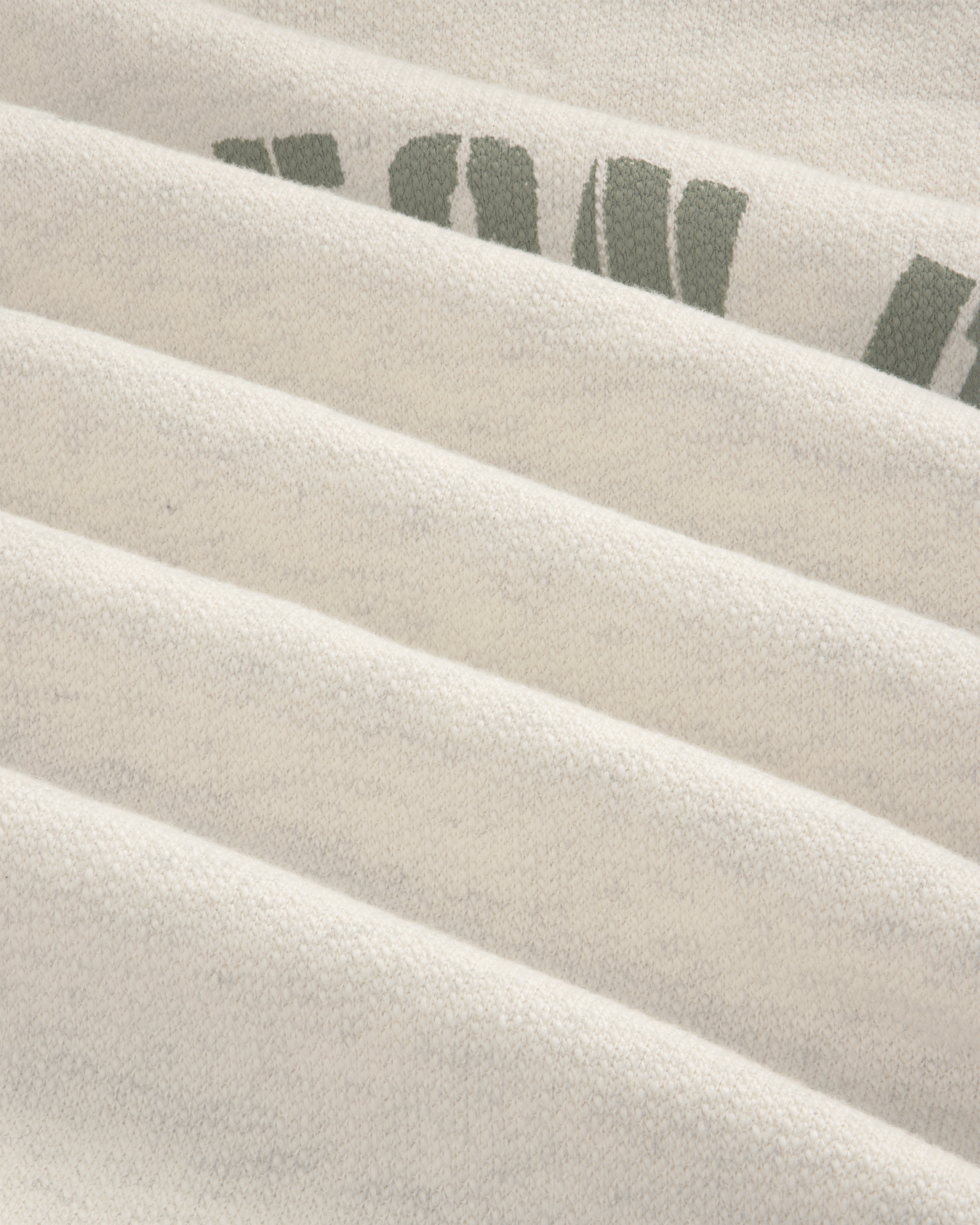 Close-up of Dock Hoodie’s light fabric with faint green text, showing soft texture and horizontal folds.