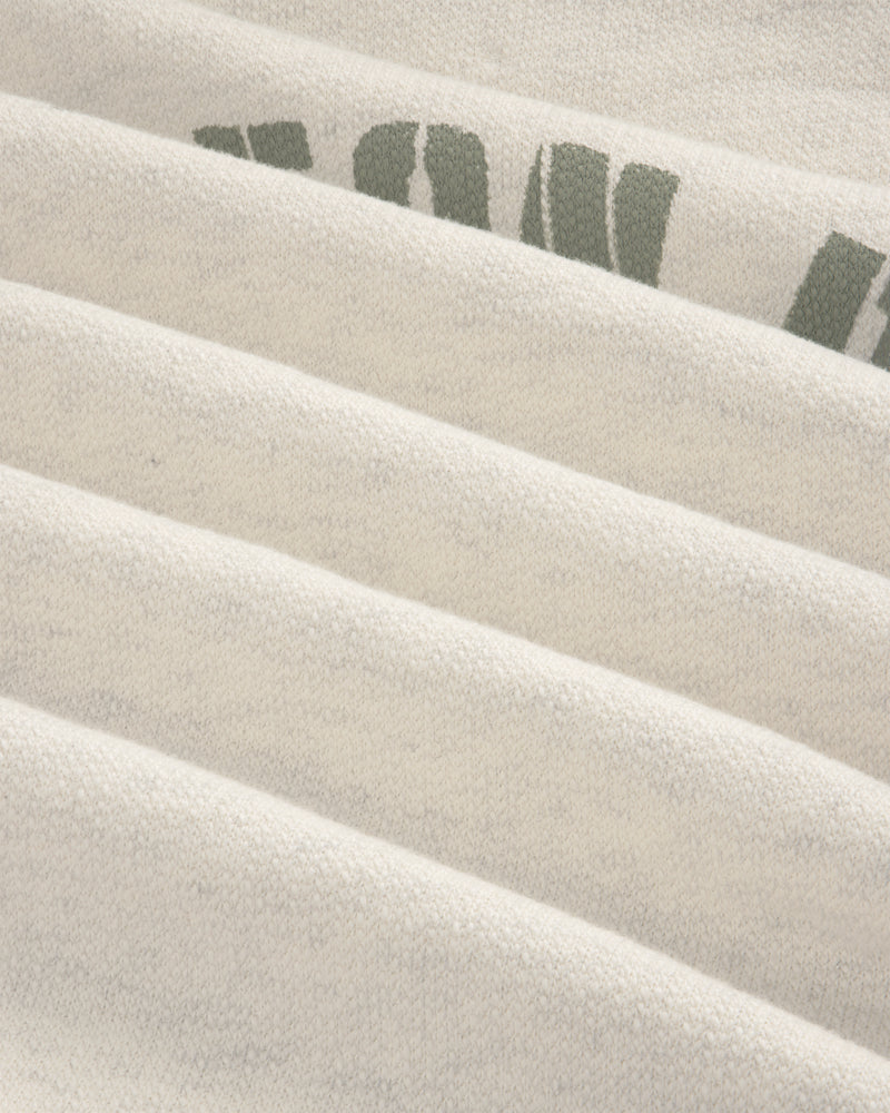 Close-up of Dock Hoodie’s light fabric with faint green text, showing soft texture and horizontal folds.