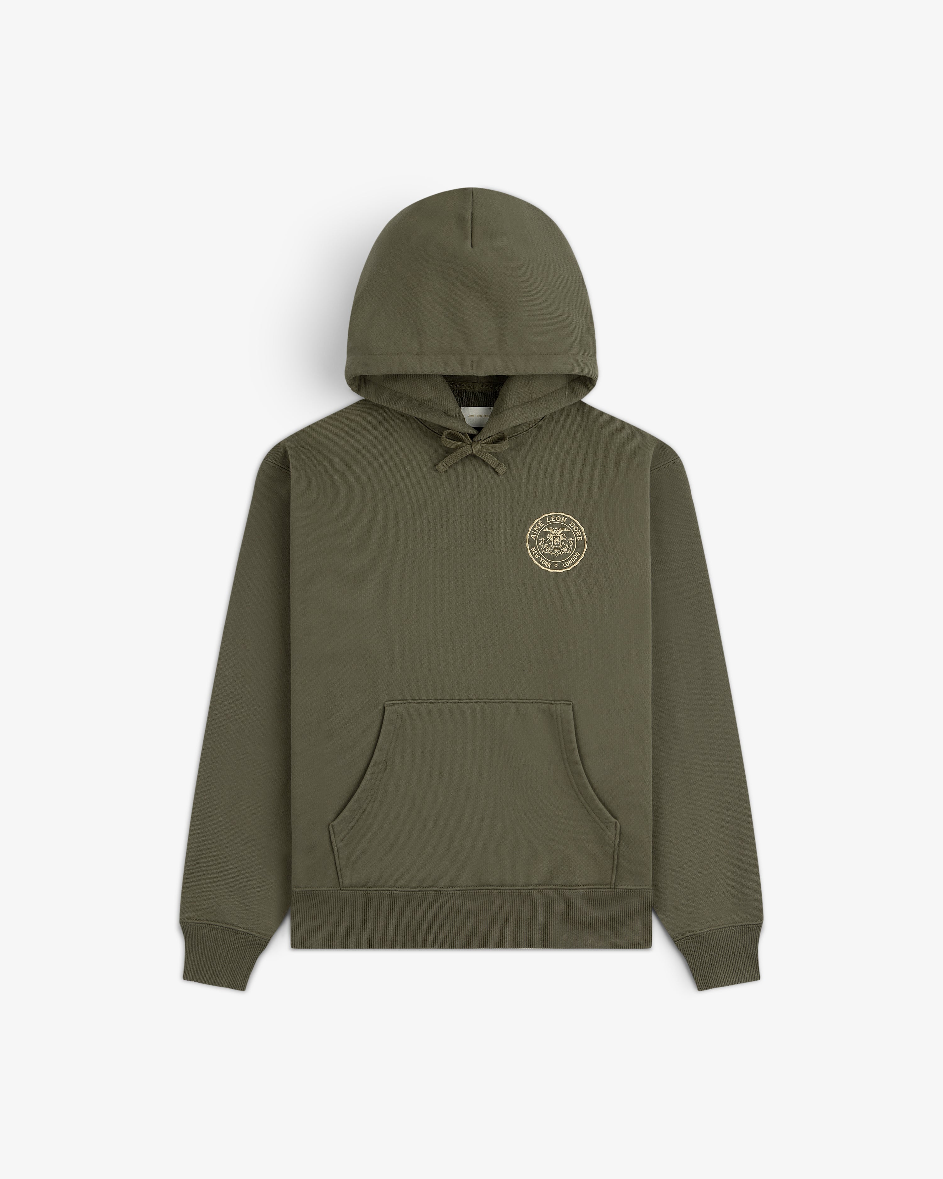 Signet Logo Hoodie in olive green with front pocket and small circular gold emblem on the left chest.