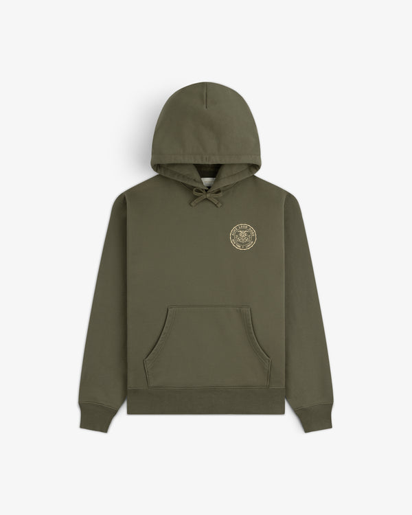Signet Logo Hoodie in olive green with front pocket and small circular gold emblem on the left chest.