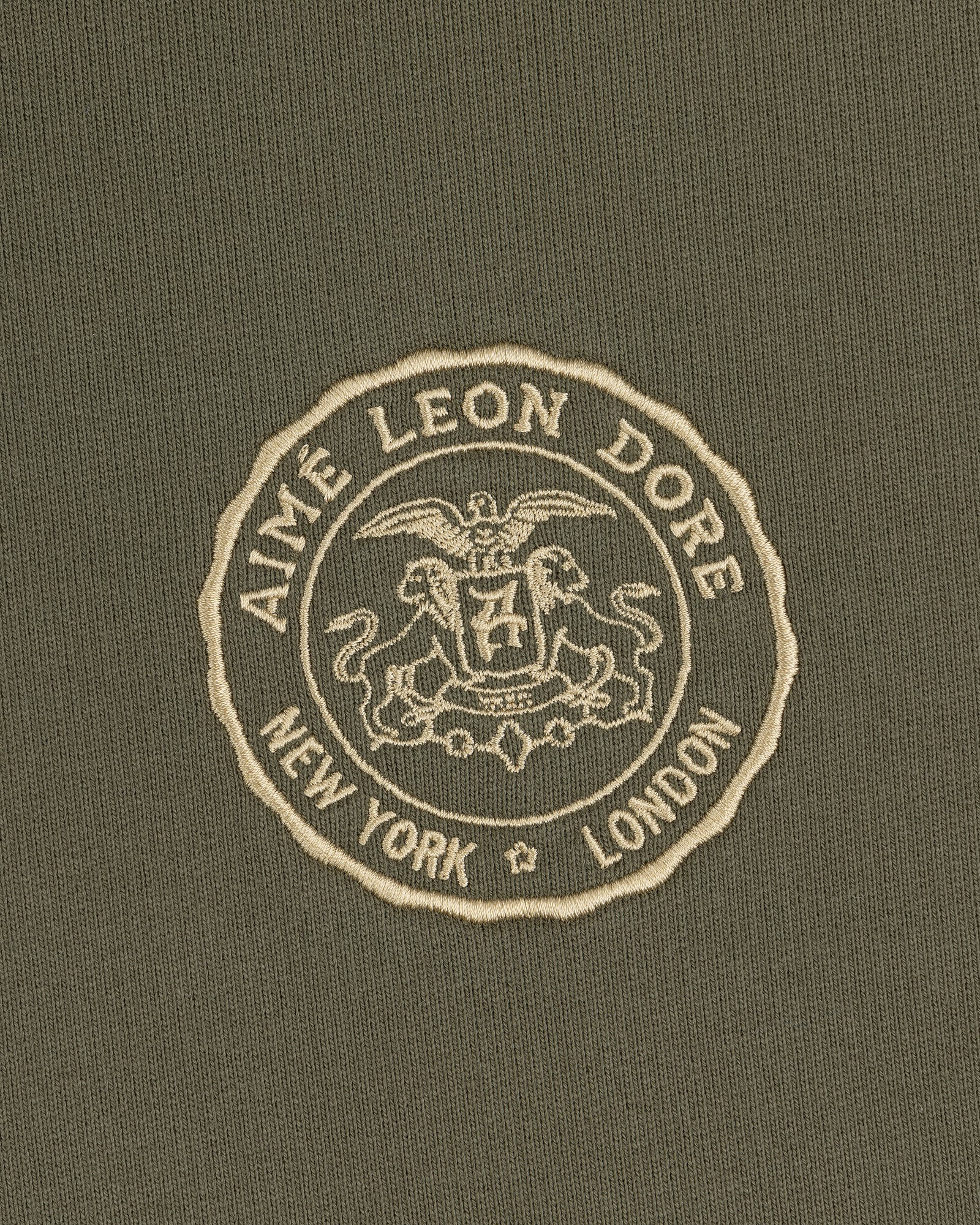 The Signet Logo Hoodie features an embossed Aimé Leon Dore crest with eagle, lion, and New York London on olive green.