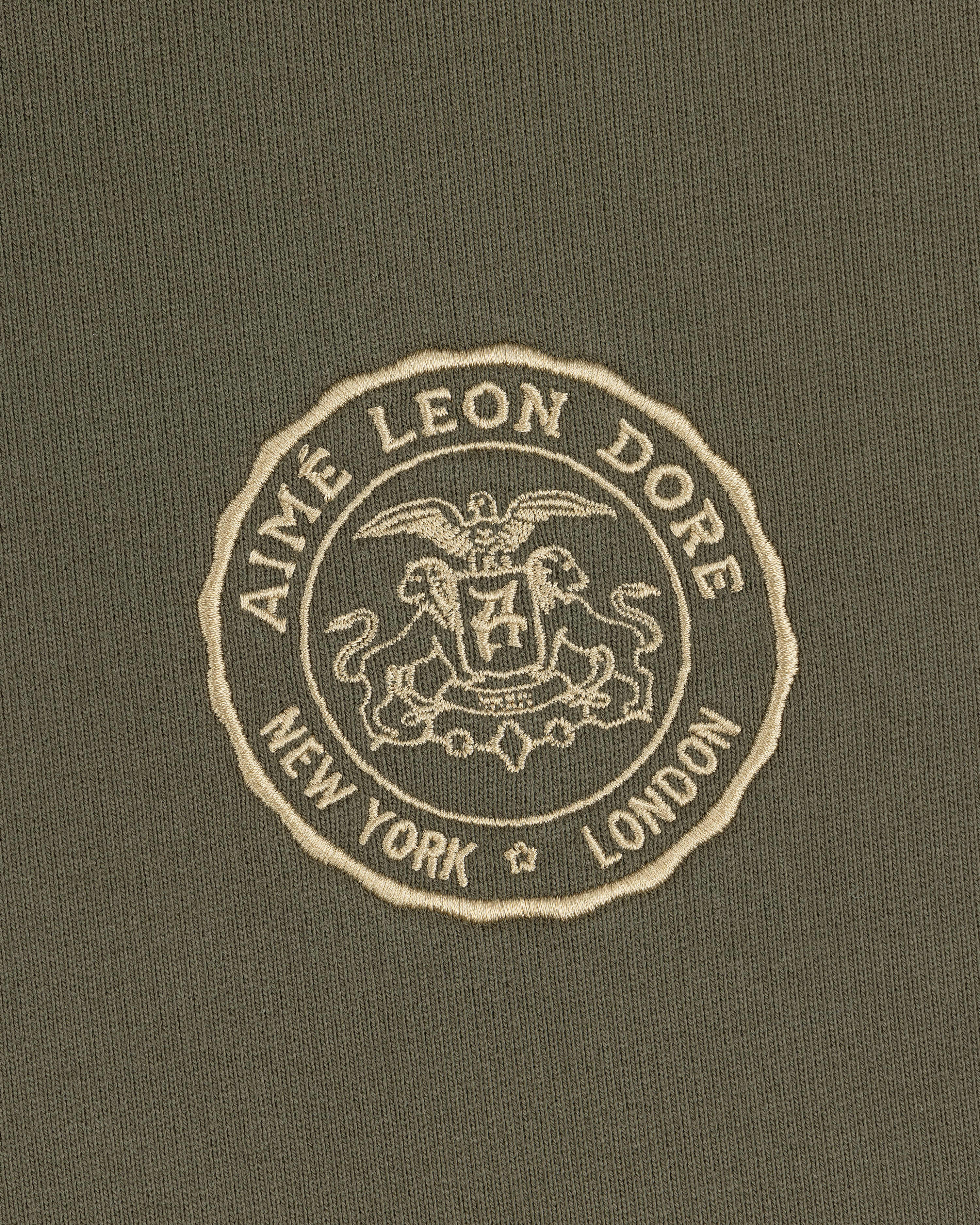 The Signet Logo Hoodie features an embossed Aimé Leon Dore crest with eagle, lion, and New York London on olive green.