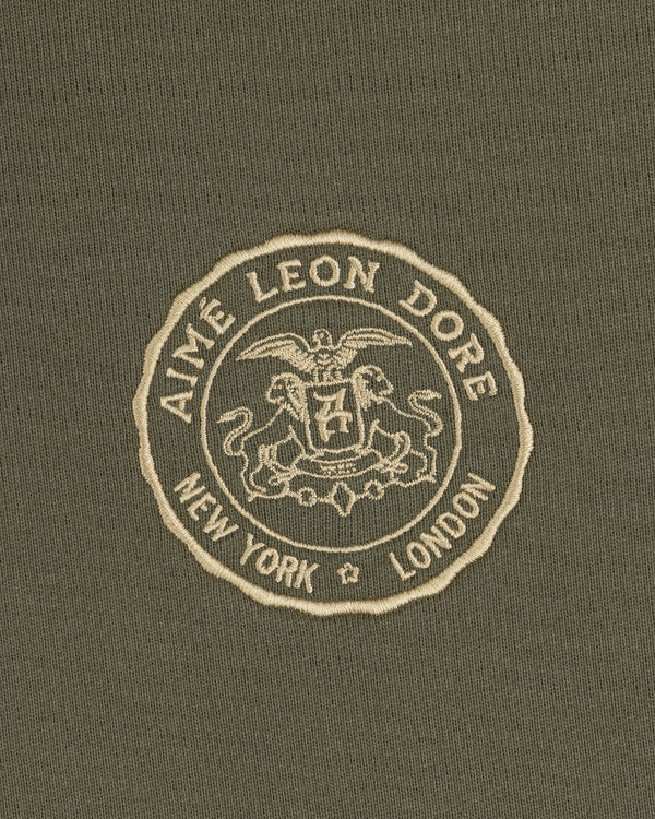 The Signet Logo Hoodie features an embossed Aimé Leon Dore crest with eagle, lion, and New York London on olive green.