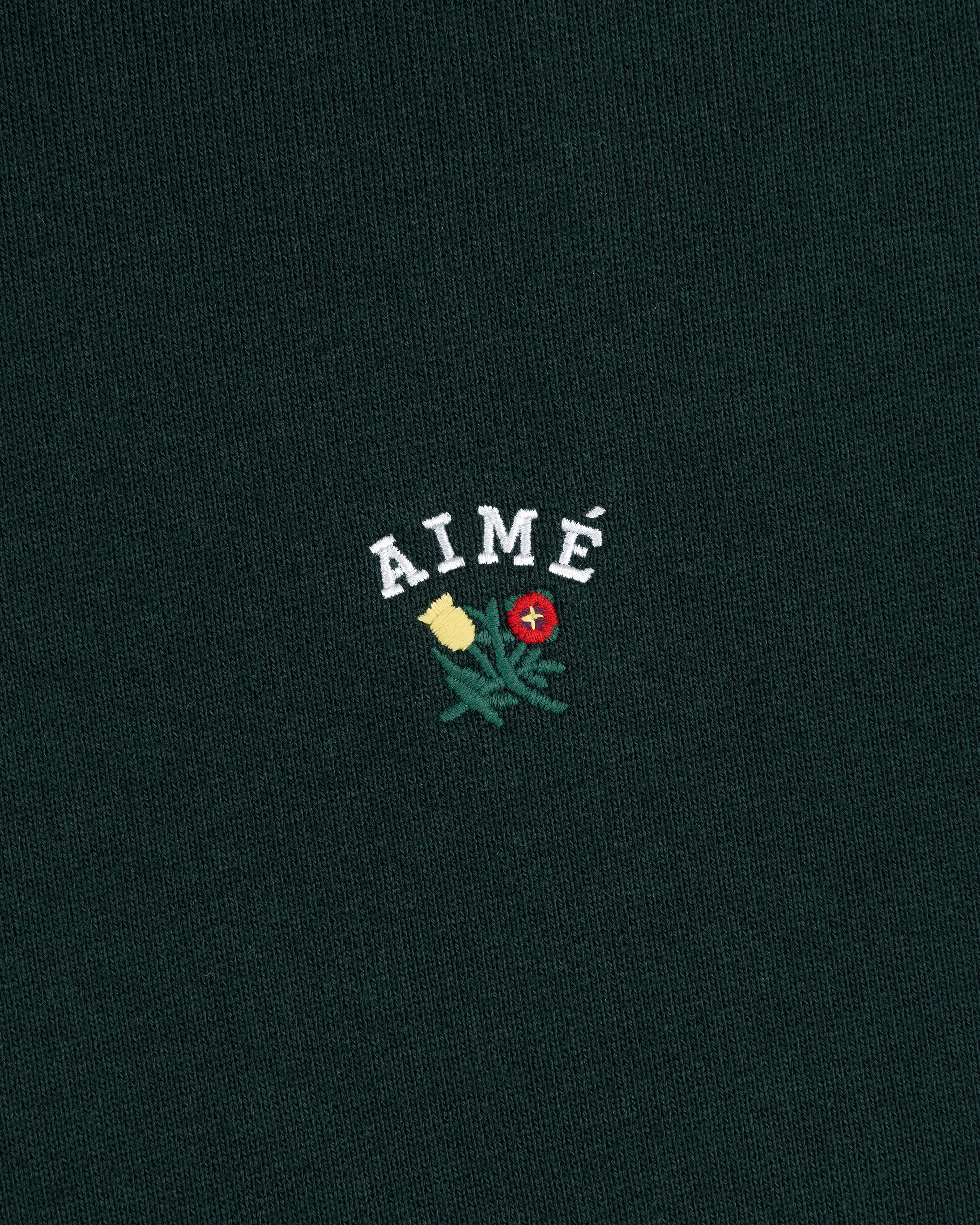 Green Crest Hoodie with AIMÉ embroidered above yellow and red flowers with green leaves.